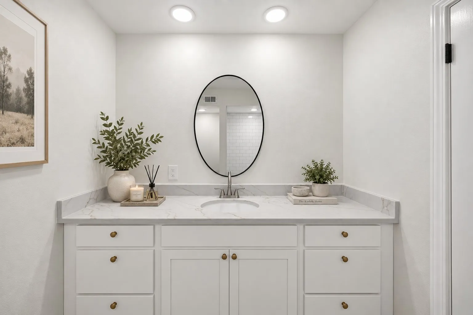 White vanity cabinetry with brass hardware, a white countertop, an undermount sink, and an oval mirror