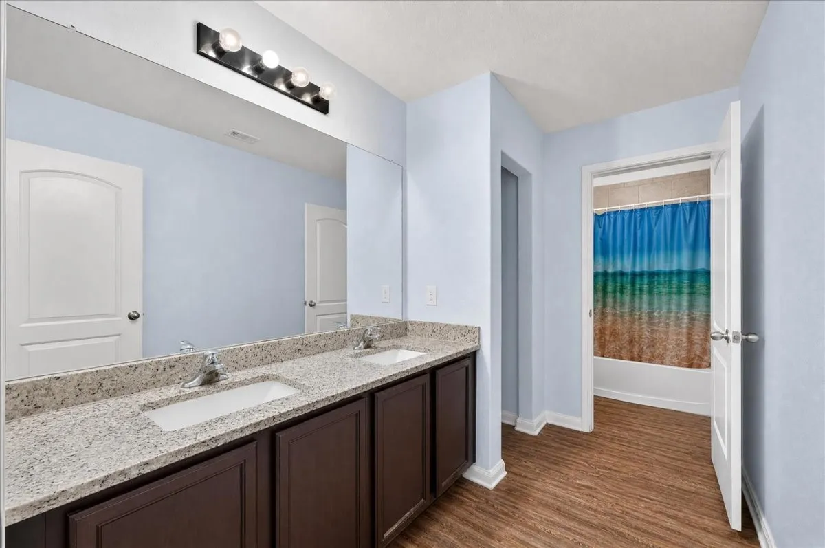 Dual vanity with undermount sinks, speckled countertop, dark wood-finish cabinetry, and a large wall-mounted mirror