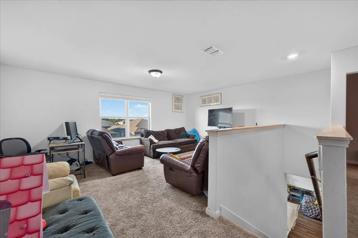 Spacious recreational room featuring expansive windows with natural light, wood-finish flooring, neutral wall finishes, and multiple functional zones for entertainment and work