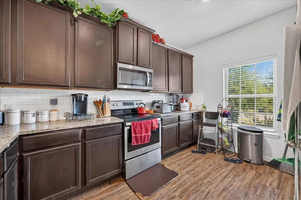 Kitchen featuring dark wood-finish cabinetry, light-toned countertops, white subway tile backsplash, stainless steel appliances, and wood-finish flooring