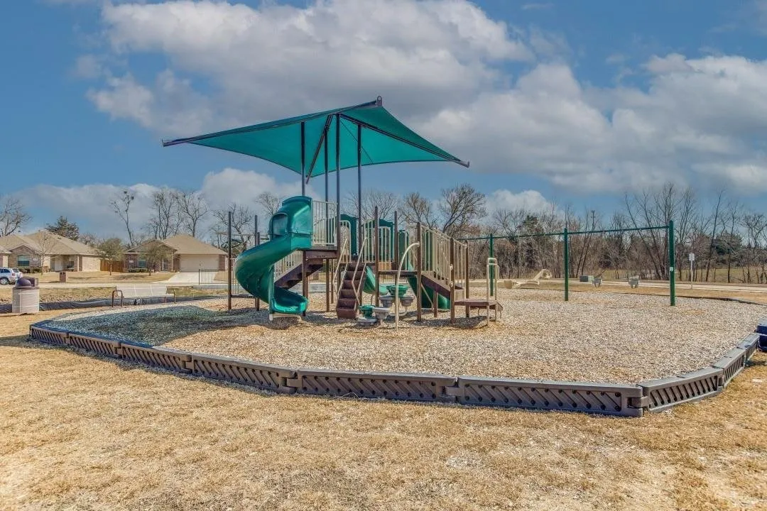 Community playground featuring a multi-level play structure with slides, swings, and a protective shade canopy