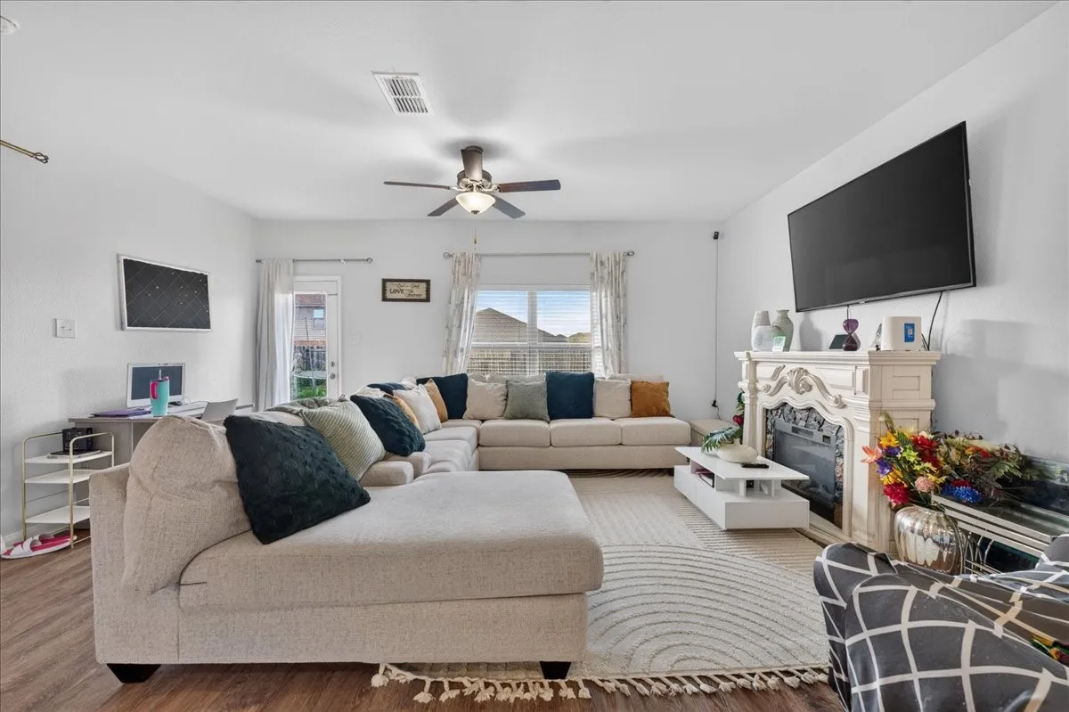 Bright living area featuring wood-finish flooring, a decorative fireplace mantel, and ceiling fan