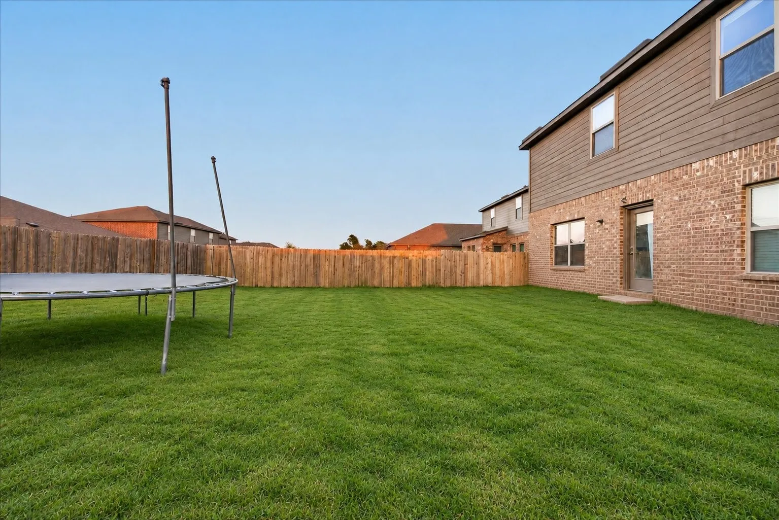 Expansive fenced backyard featuring a grassy lawn, brick exterior, and horizontal siding
