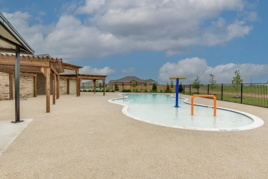 Expansive pool area featuring a freeform swimming pool, integrated splash pad, and surrounding aggregate decking