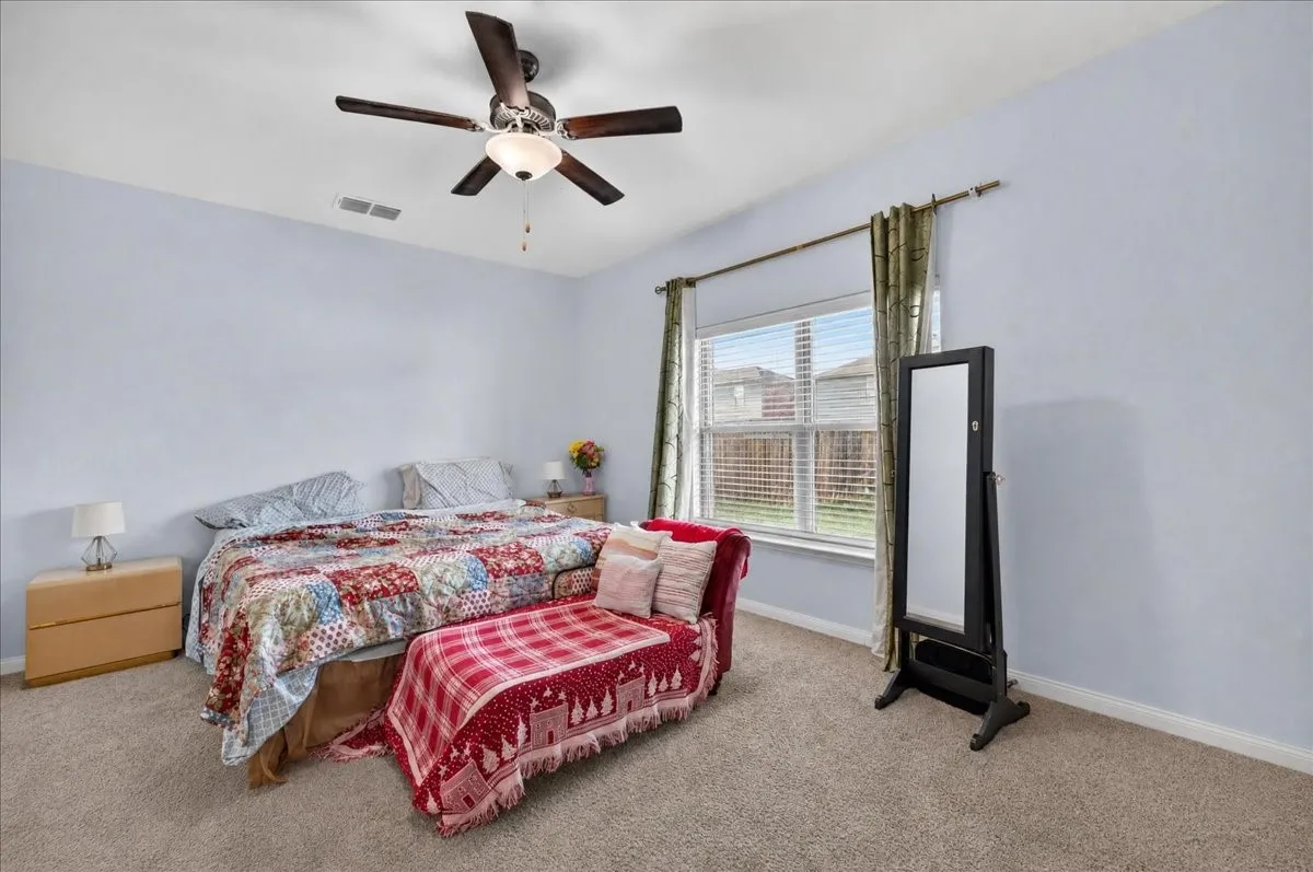 Carpeted room with a ceiling fan light fixture and a window featuring blinds and drapes