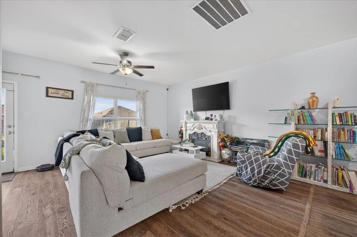Wood-finish flooring throughout, ceiling fan with integrated lighting, window with ample natural light, and a decorative fireplace