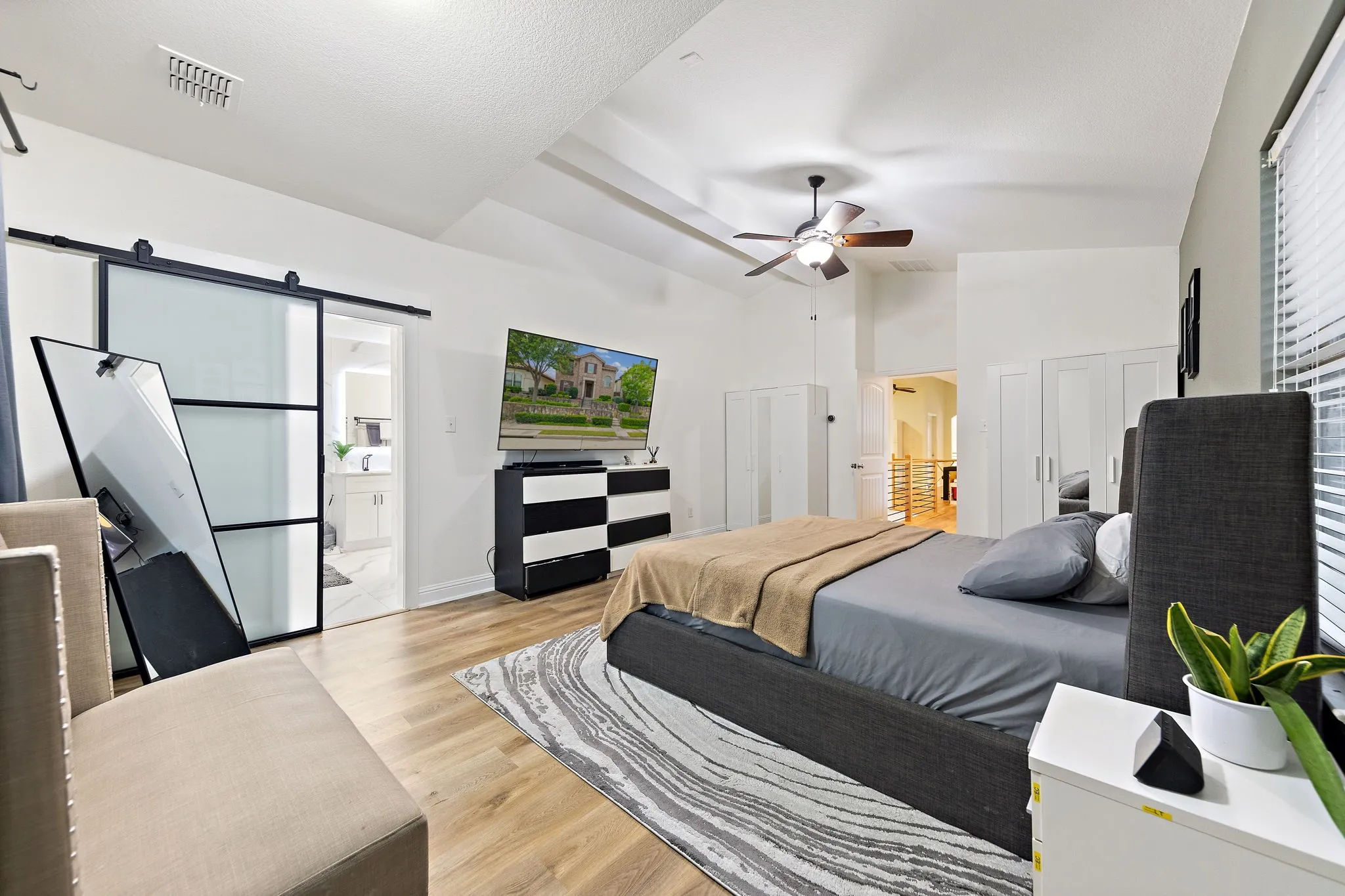 Vaulted ceiling with ceiling fan, wood-finish flooring, sliding barn door with frosted panels, and built-in cabinetry