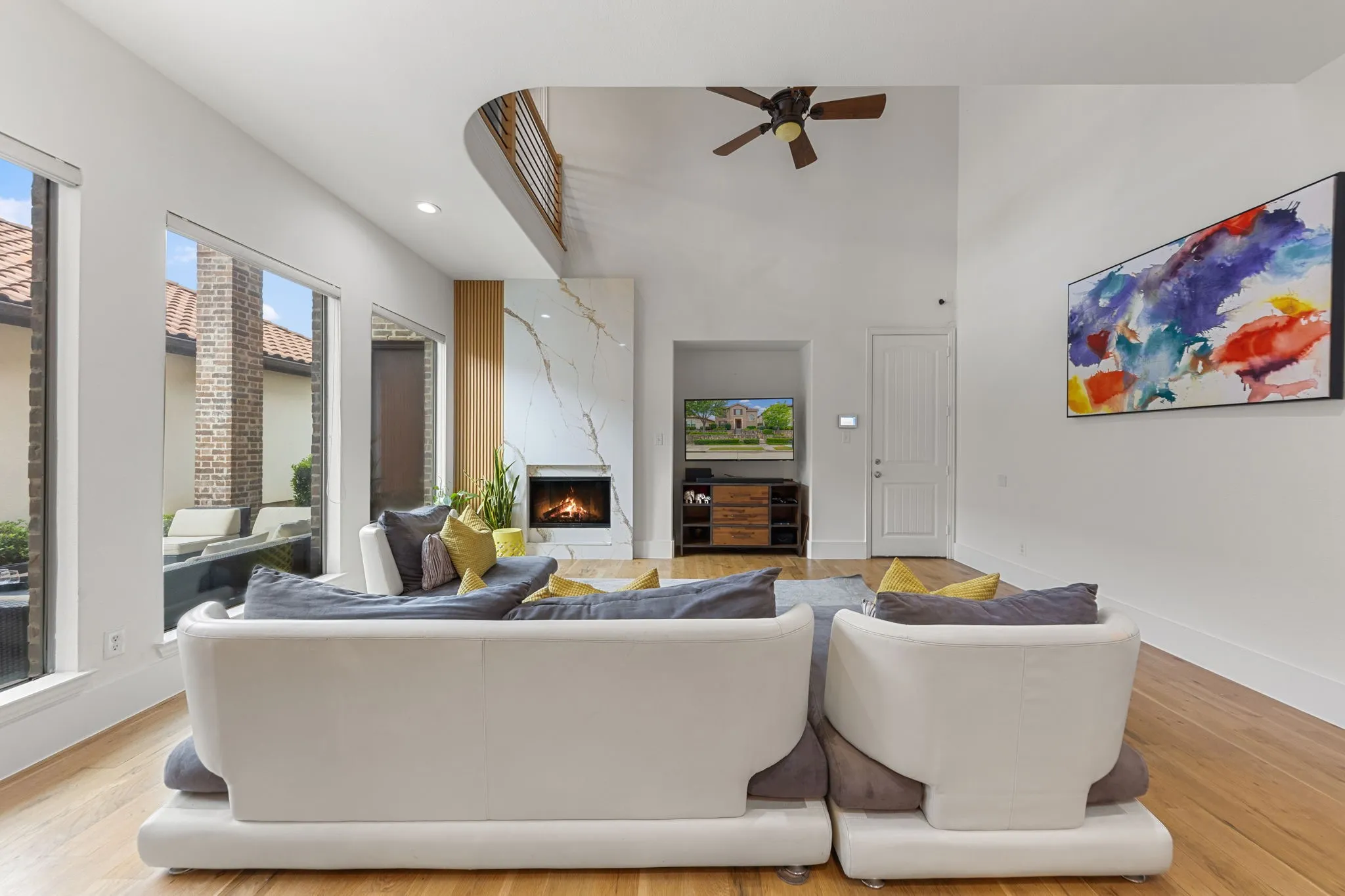 Vaulted ceiling living area with wood-finish flooring, a contemporary fireplace with a large stone surround, and expansive windows