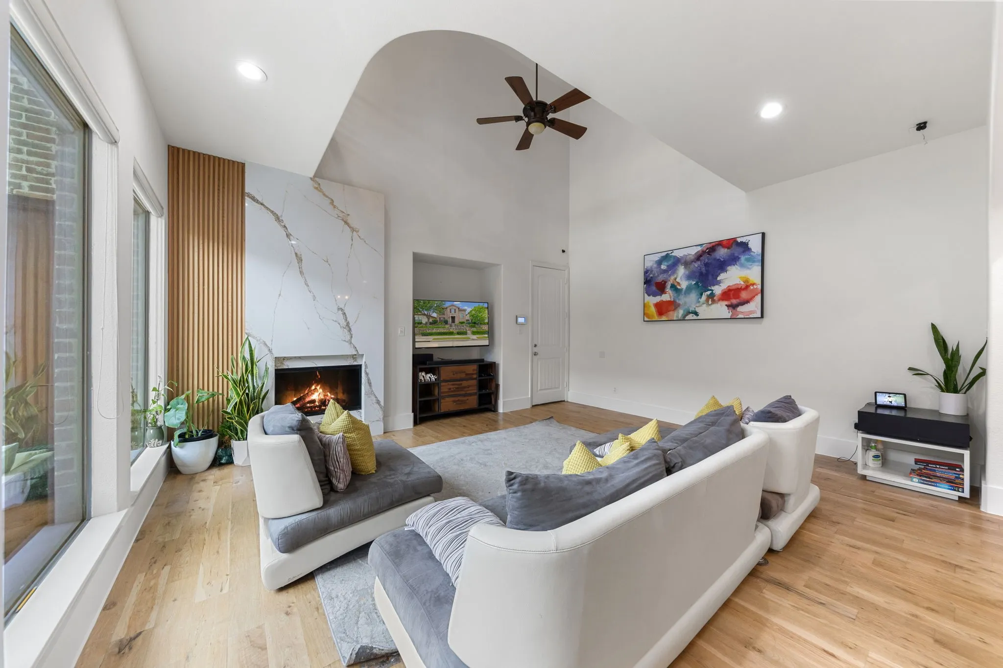 Vaulted ceiling with recessed lighting, wood-finish flooring, full-height stone fireplace, wood slat accent wall, and expansive window