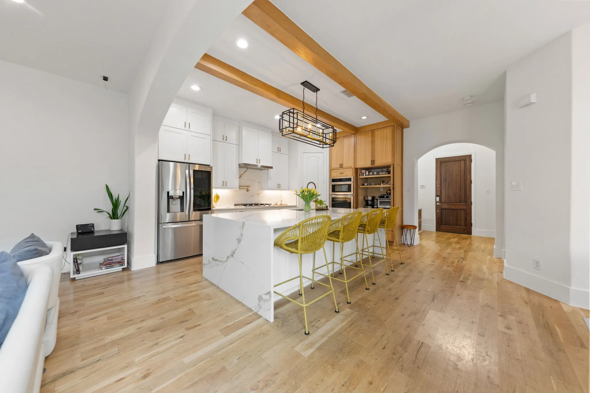 Gourmet kitchen featuring a large waterfall island with seating, stainless steel appliances, wood-finish flooring, white cabinetry, and wood beam accents