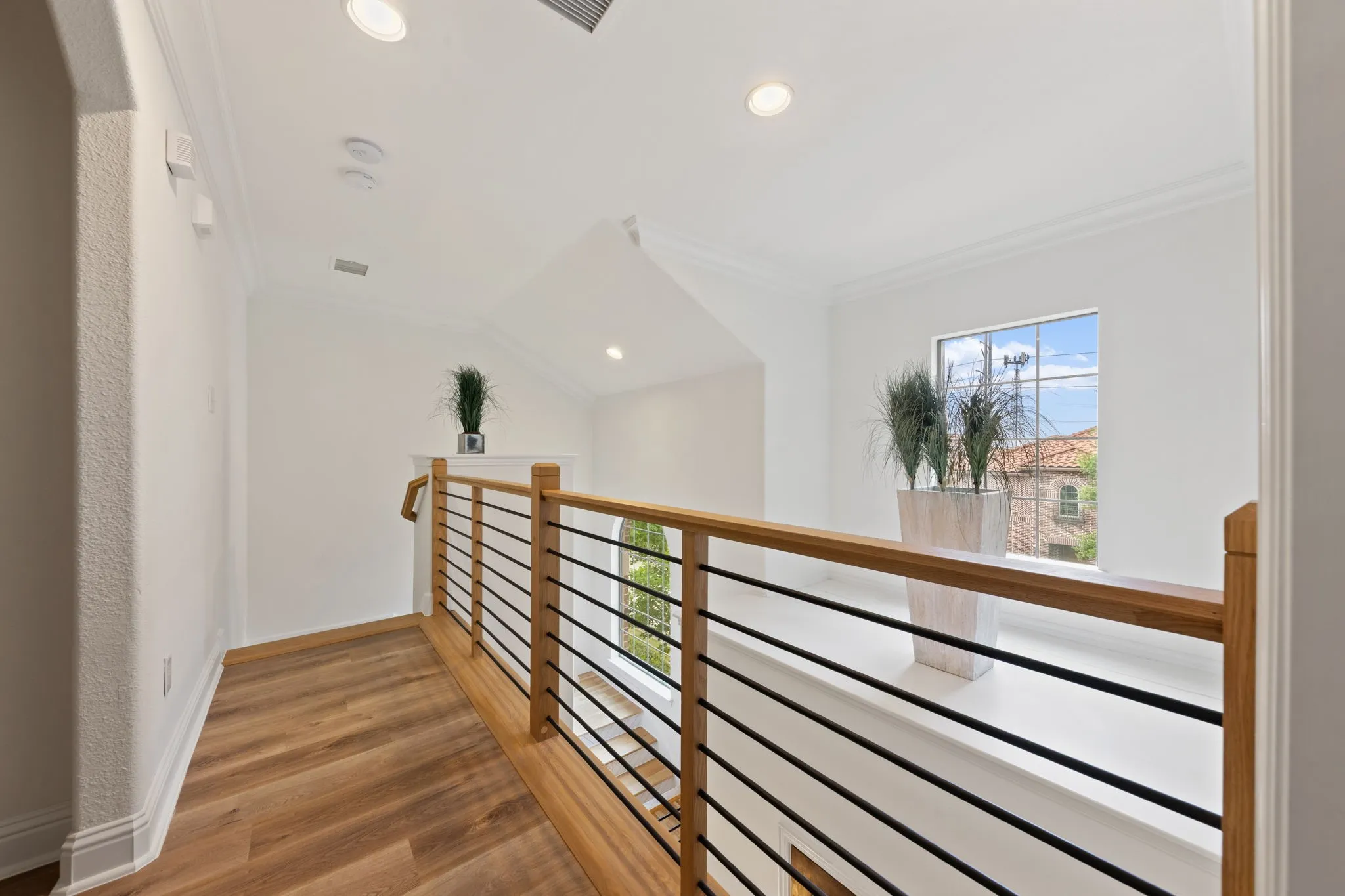 Wood-finish flooring, recessed lighting, crown molding, a window with exterior views, and a wood and metal railing