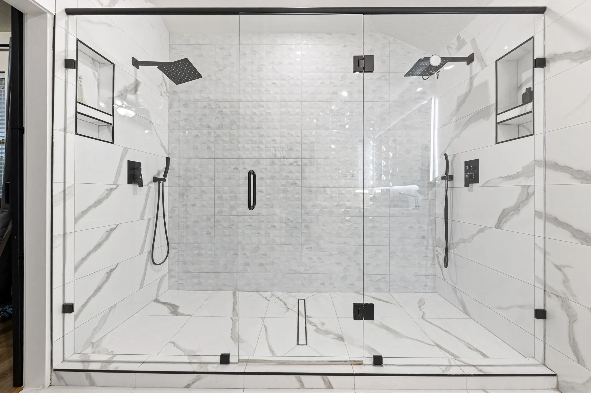 Glass-enclosed shower with contrasting white and textured wall tiles, dual rainfall showerheads, and integrated wall niches