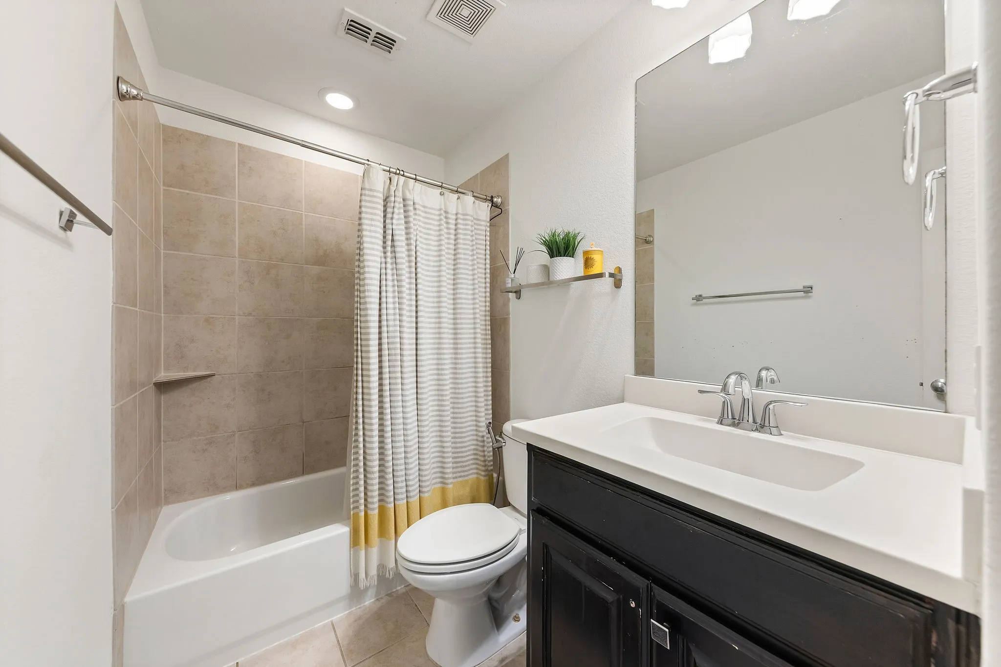 White bathtub with tiled surround, recessed lighting, and a dark wood vanity with white countertop