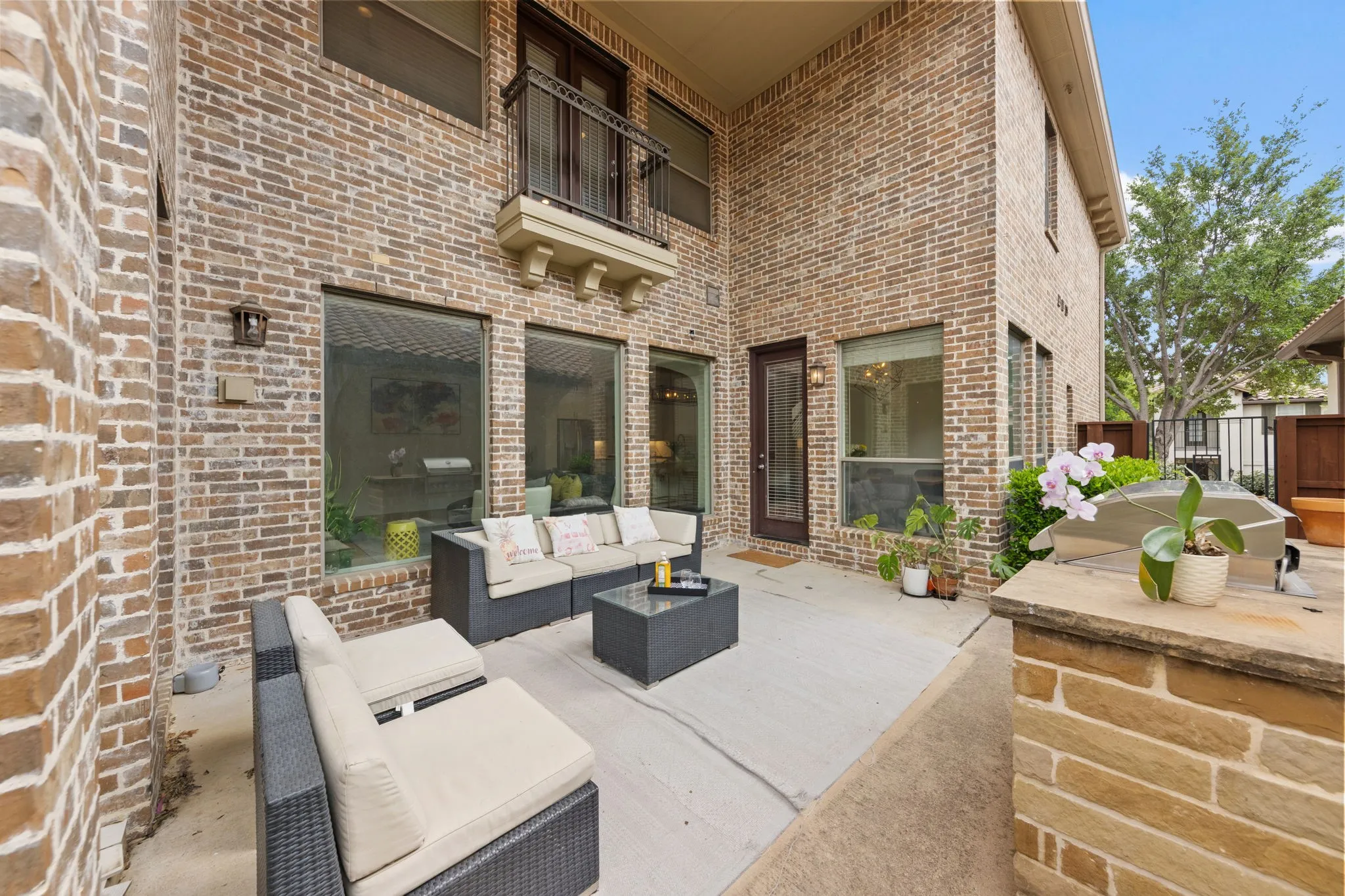 Private outdoor patio with brick exterior, large windows, and an upper-level balcony with iron railing