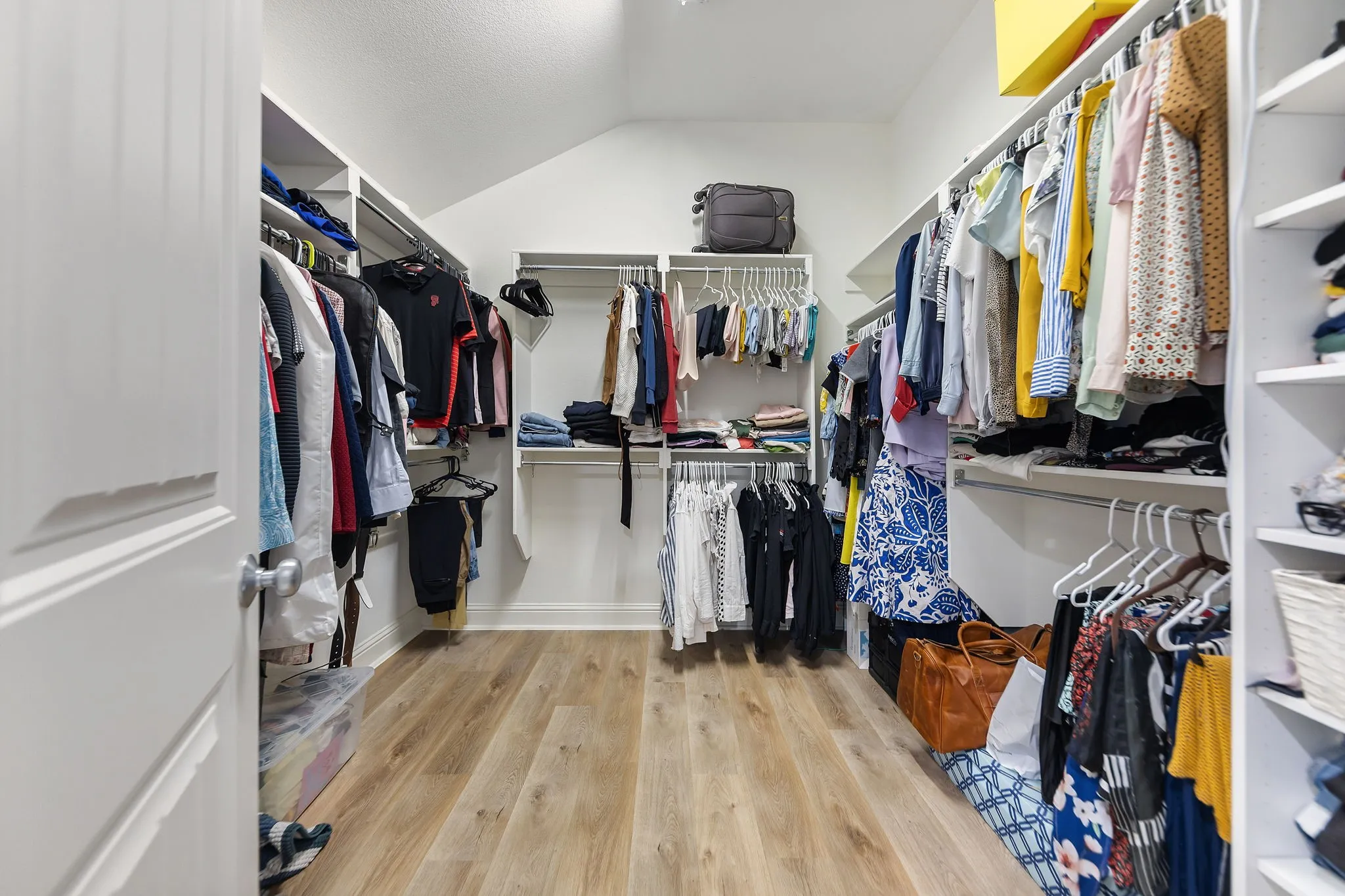 Walk-in closet featuring wood-finish flooring, white shelving, and multiple clothing rods