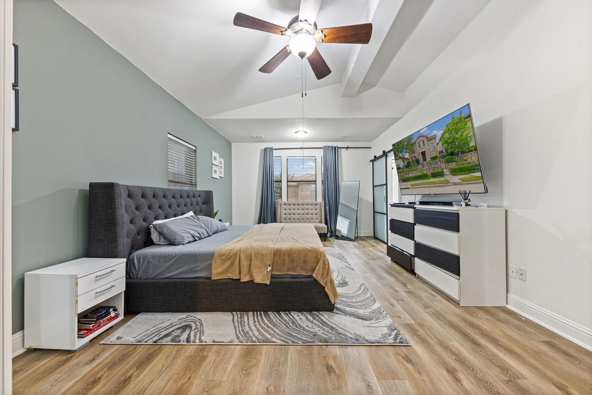 Vaulted ceiling with a ceiling fan, light wood-finish flooring, and a sliding barn door