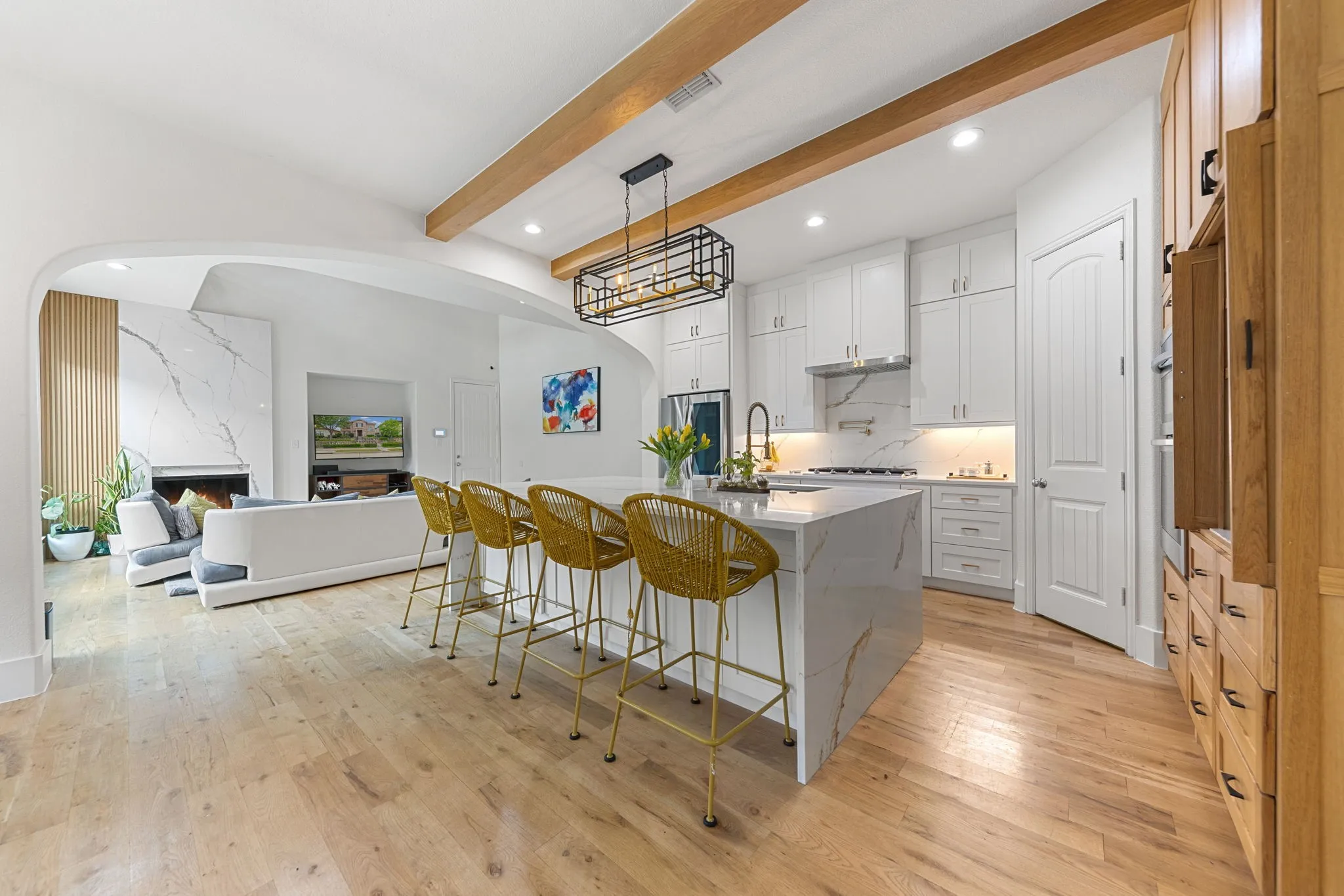 Kitchen with a large waterfall island featuring a stone-finish countertop, white cabinetry with under-cabinet lighting, and wood-finish flooring