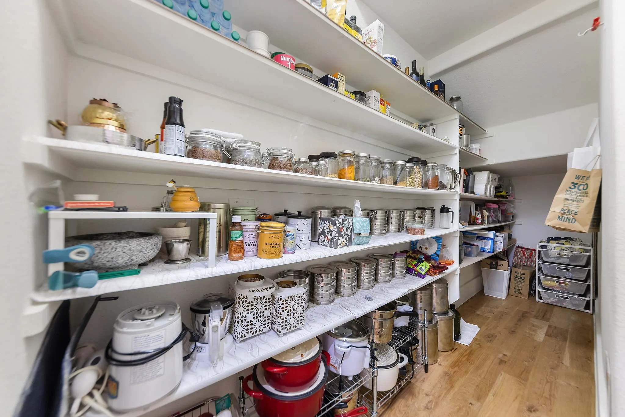 Walk-in pantry featuring extensive built-in shelving, white walls, and wood-finish flooring