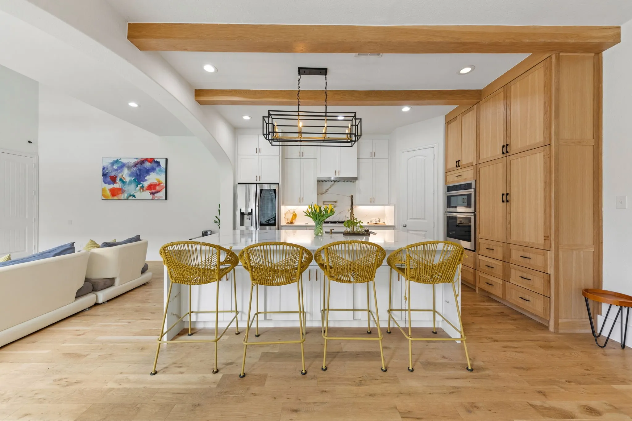 Kitchen featuring wood-finish flooring, wood beam accents, a central island with countertop seating, stainless steel double ovens, and extensive built-in cabinetry