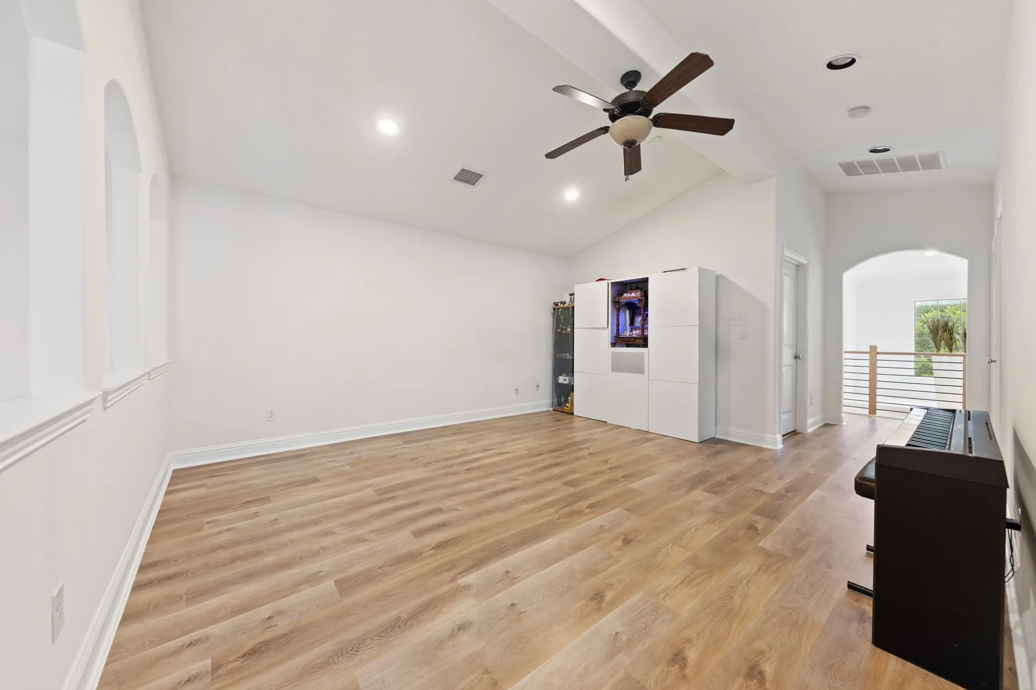 Vaulted ceiling with a ceiling fan, recessed lighting, wood-finish flooring, and arched window details