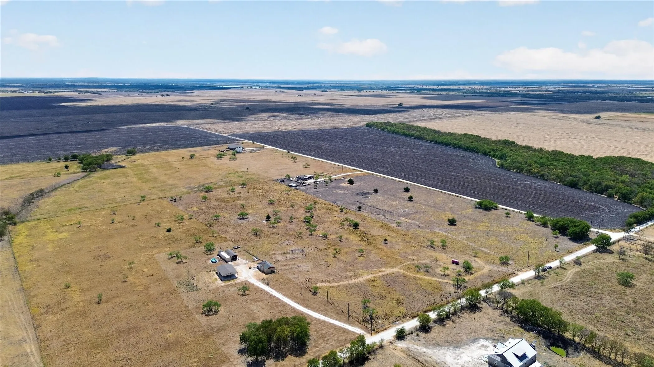 Expansive rural property featuring several structures, a gravel driveway, open fields, and mature tree lines