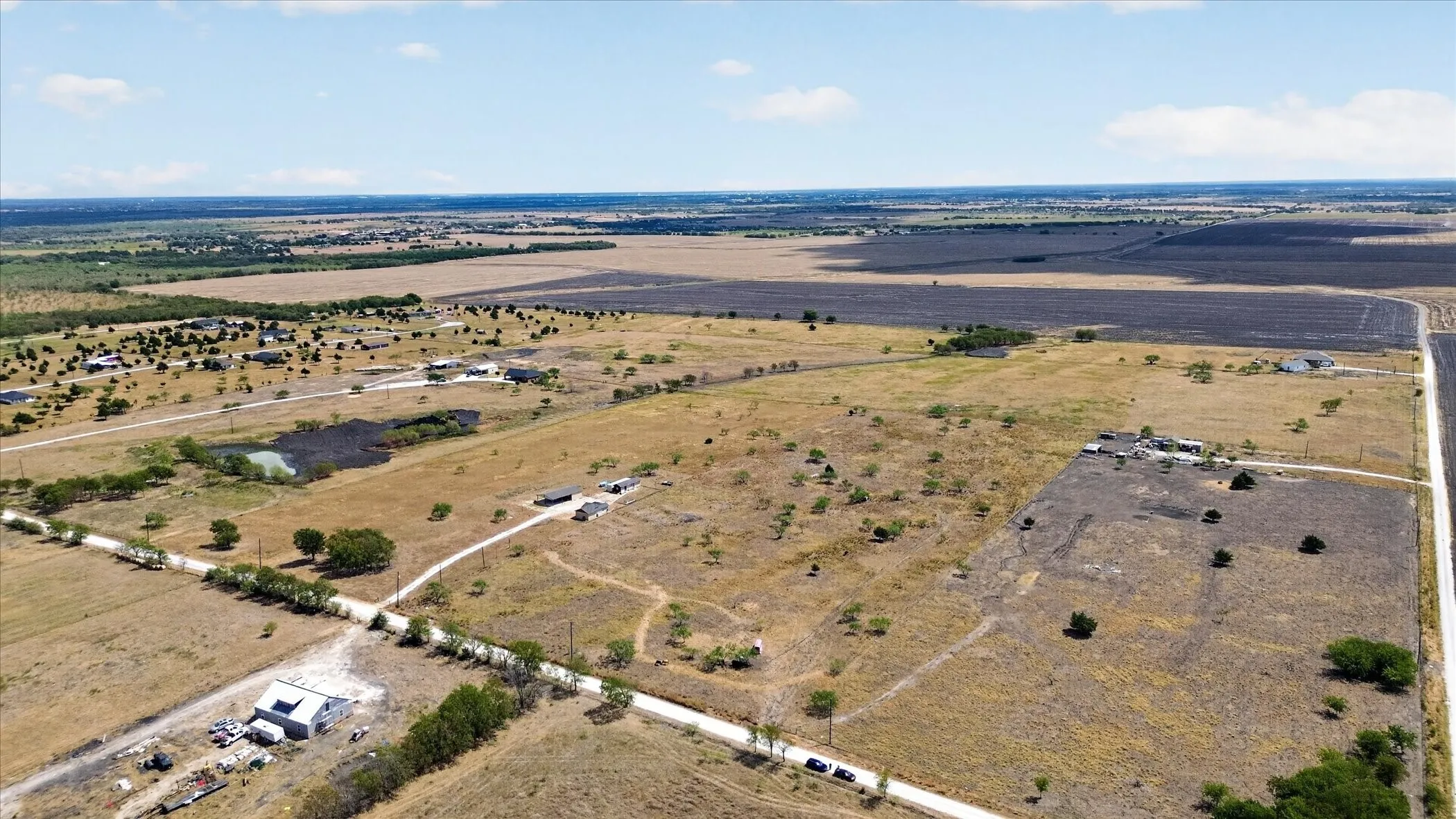Expansive rural landscape featuring a natural pond, multiple residential structures, and extensive open fields