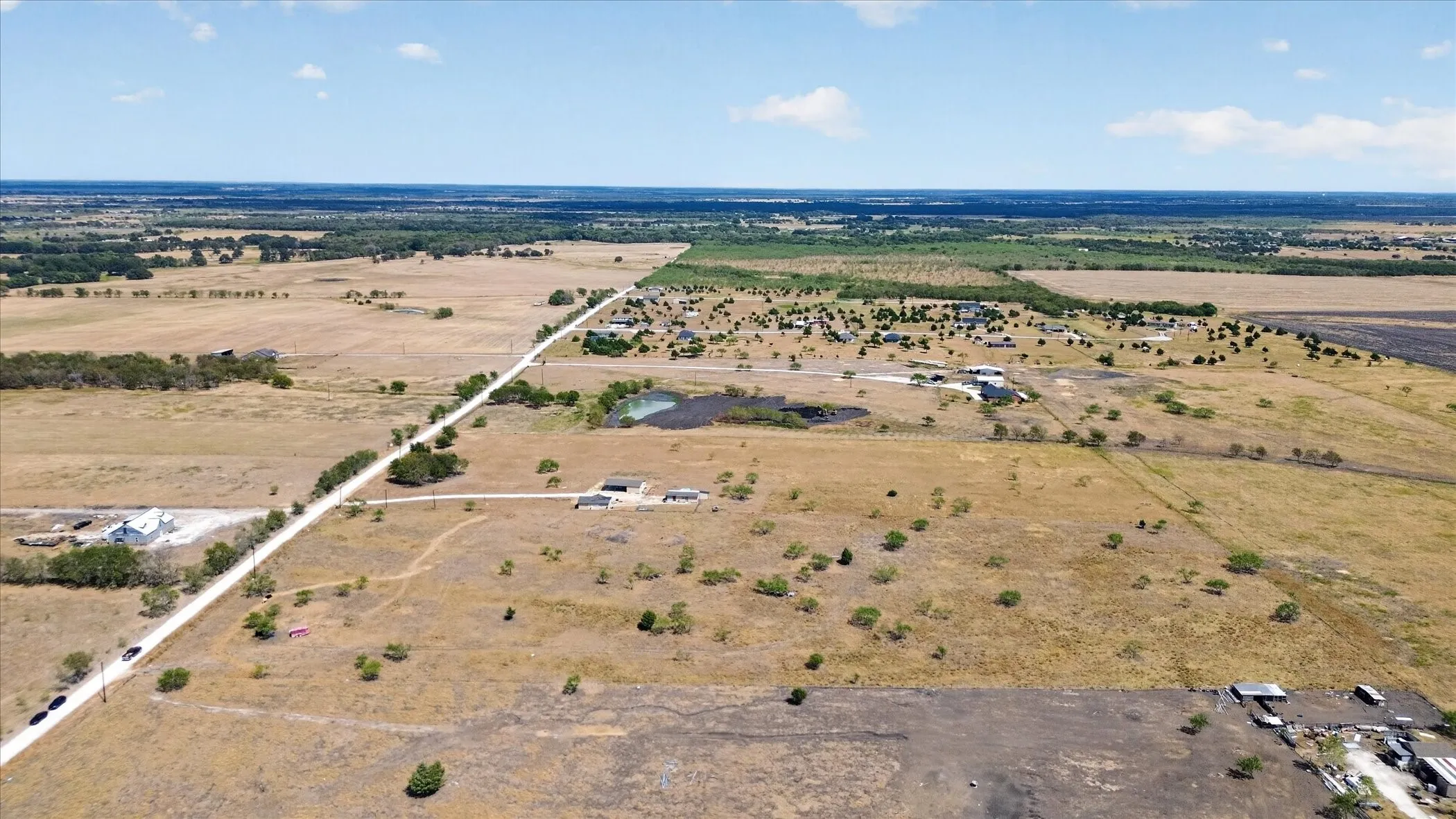 Expansive agricultural land with scattered trees, featuring a visible pond and multiple structures