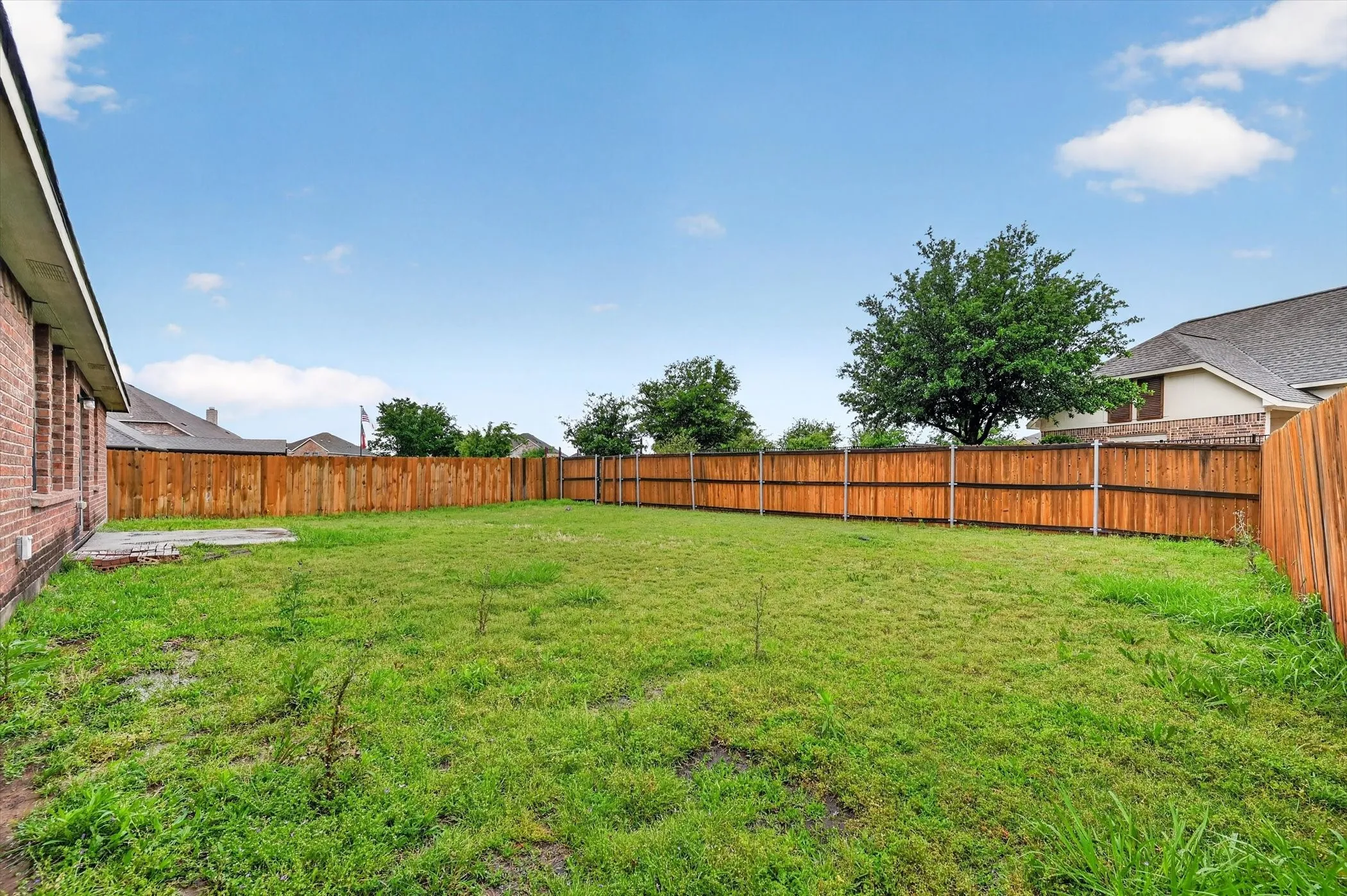 Expansive grassy backyard featuring a full perimeter privacy fence and a concrete patio pad