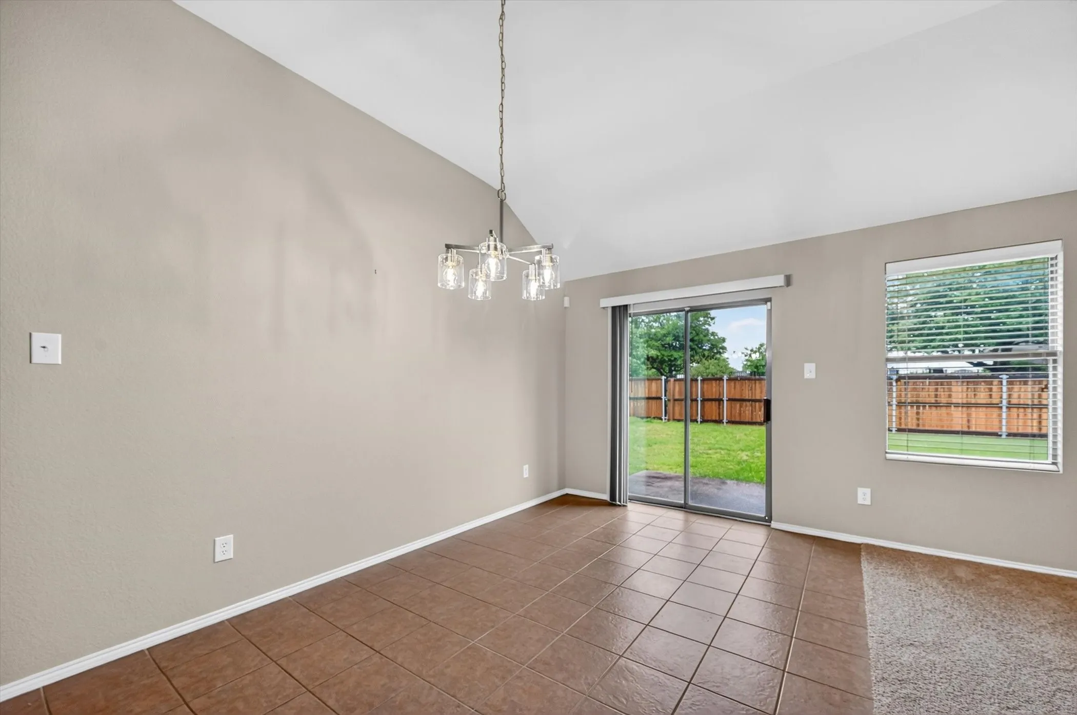 Vaulted ceiling, contemporary chandelier, tile flooring, sliding glass door, private backyard with wooden fencing