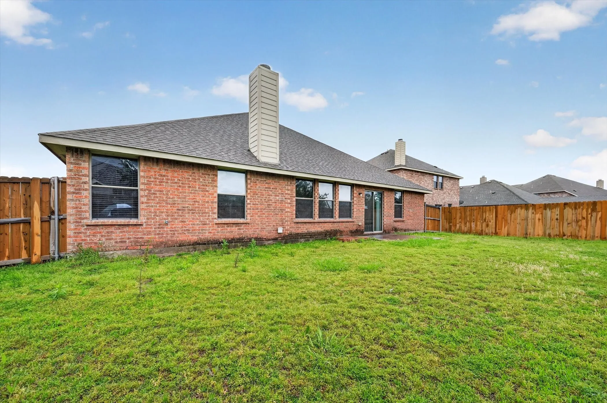 Expansive backyard with a brick exterior, multiple windows, a sliding glass door, and a wooden privacy fence