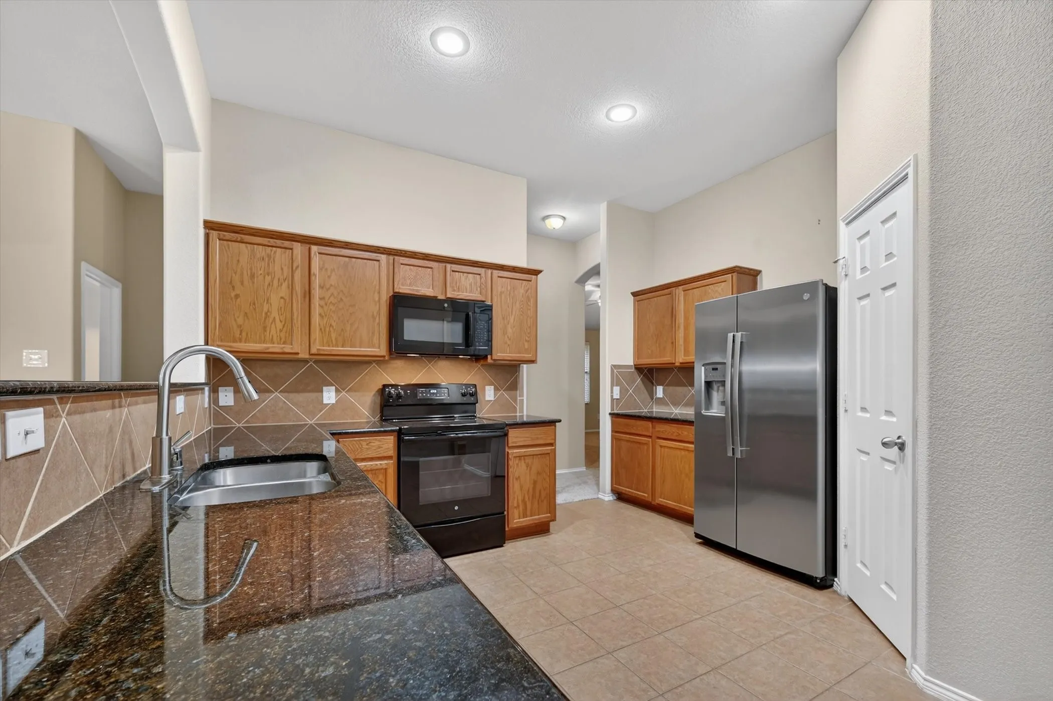 Kitchen featuring granite countertops, wood cabinetry, stainless steel appliances, a tile backsplash, and recessed lighting