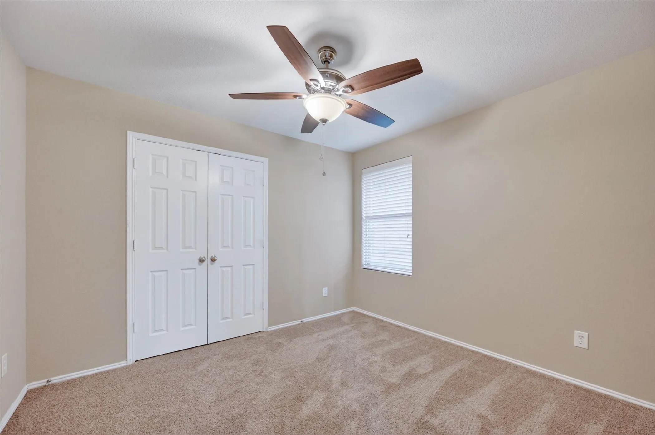 Bedroom #2 -Neutral wall color, textured carpeting, a window with blinds, and a ceiling fan with integrated lighting