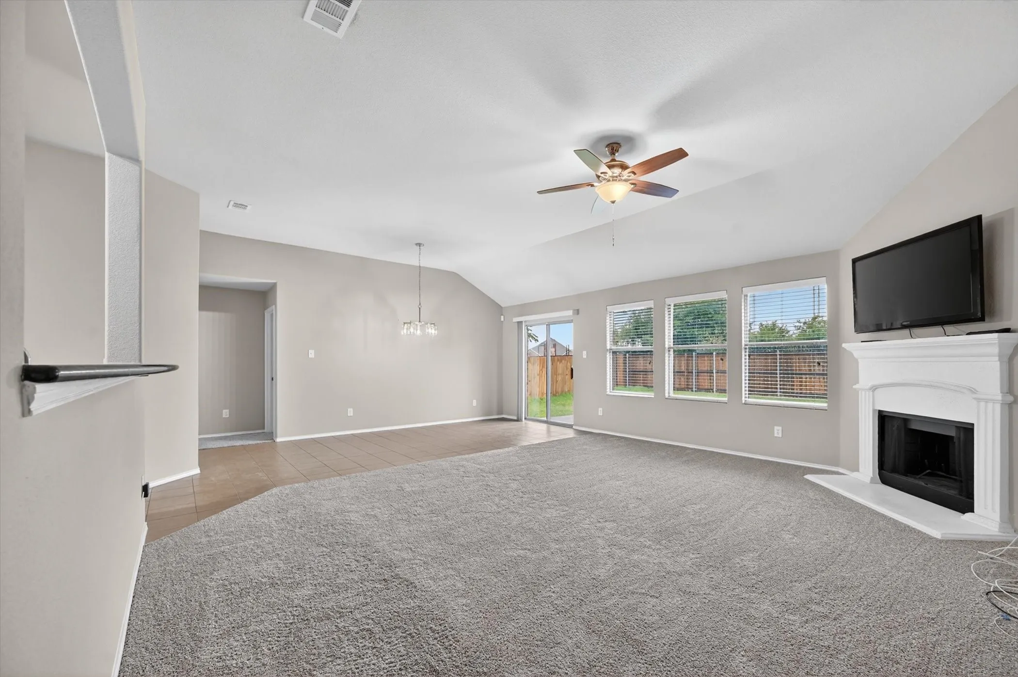 Spacious interior featuring a vaulted ceiling, ceiling fan, fireplace with mantel, and sliding glass door