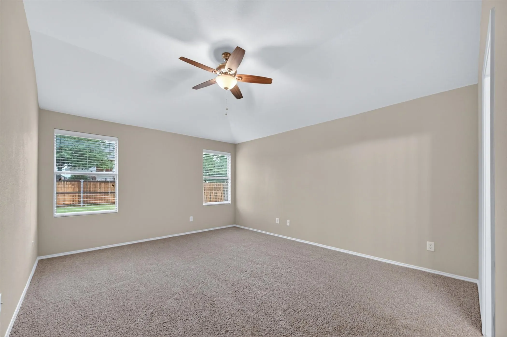 Vaulted ceiling with a ceiling fan, dual windows with blinds, and neutral-toned wall paint