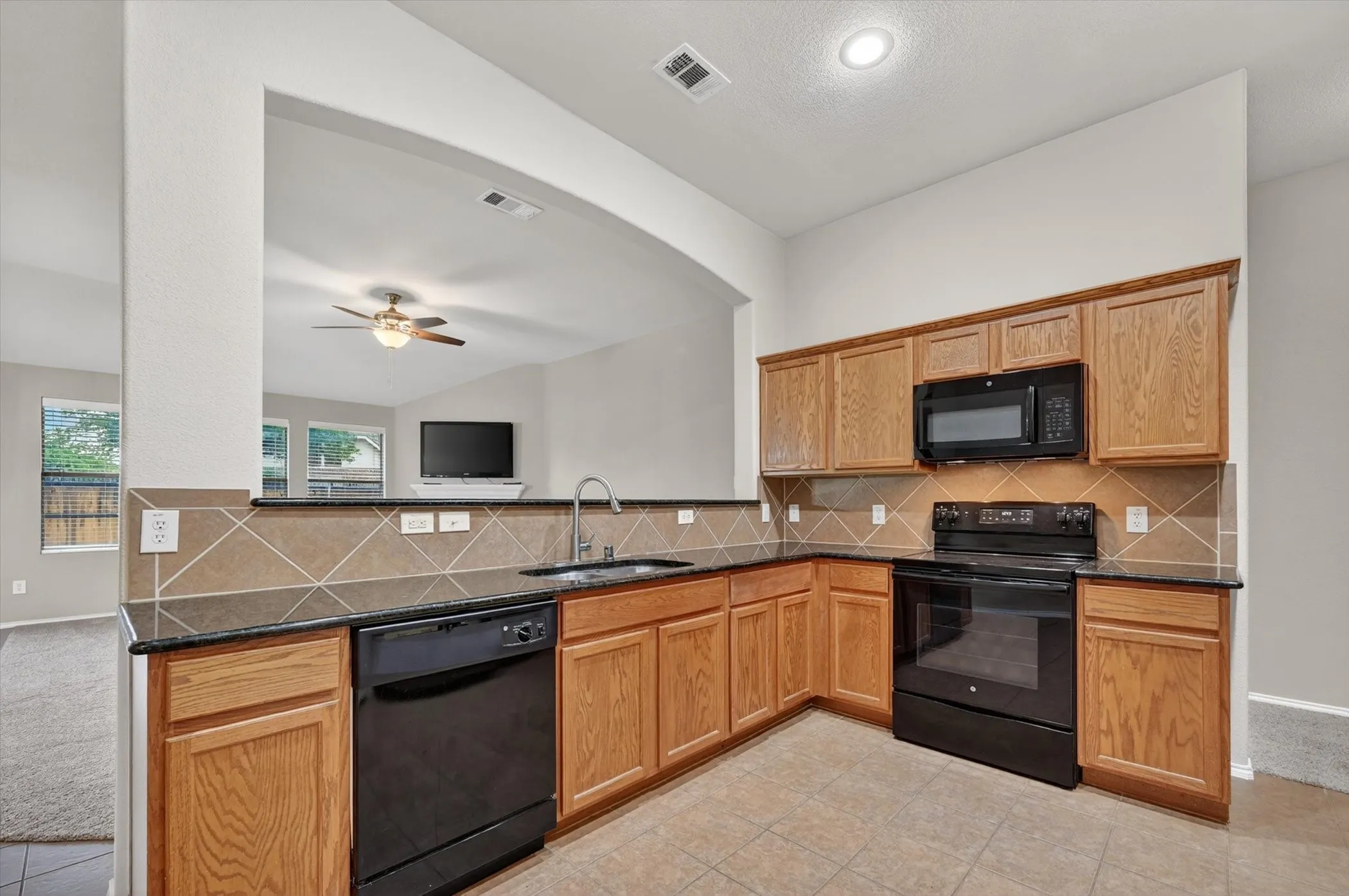 Kitchen featuring wood-finish cabinetry, black appliances, dark countertops, and a tiled backsplash