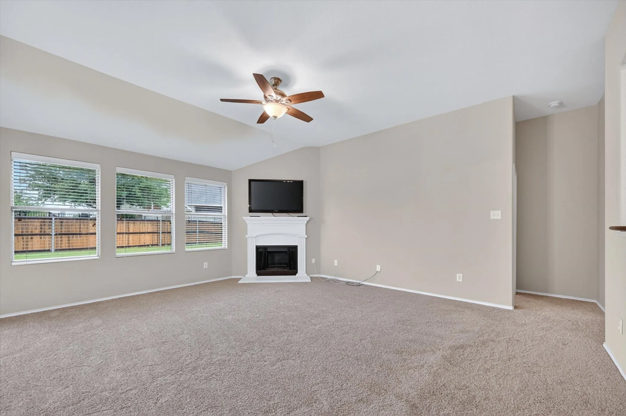 Vaulted ceiling, ceiling fan with integrated lighting, multiple windows, fireplace with mantel, and carpeting
