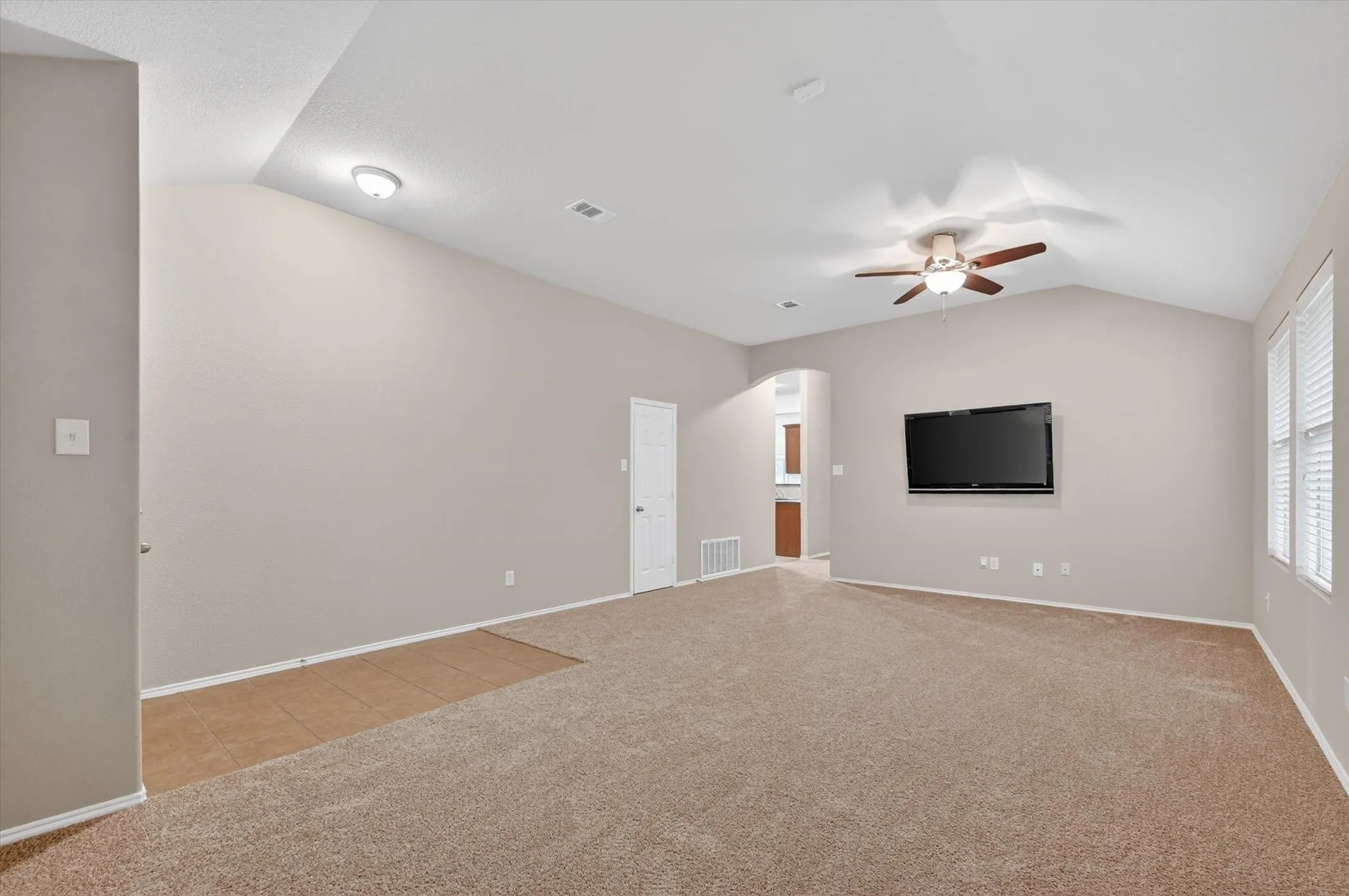 Vaulted ceilings, a ceiling fan with integrated lighting, and carpeted flooring with a tile entry