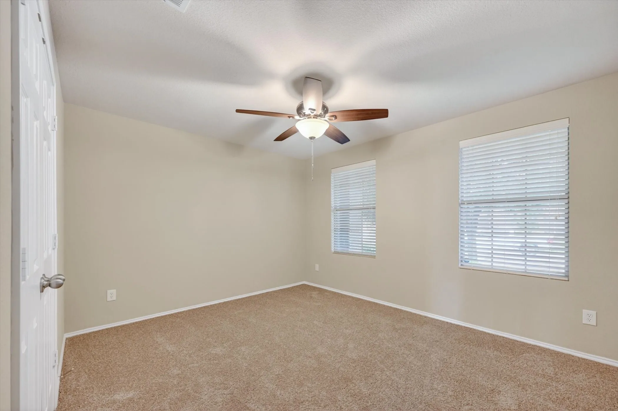 Wall-to-wall carpeting, two windows with blinds, and a ceiling fan with integrated lighting