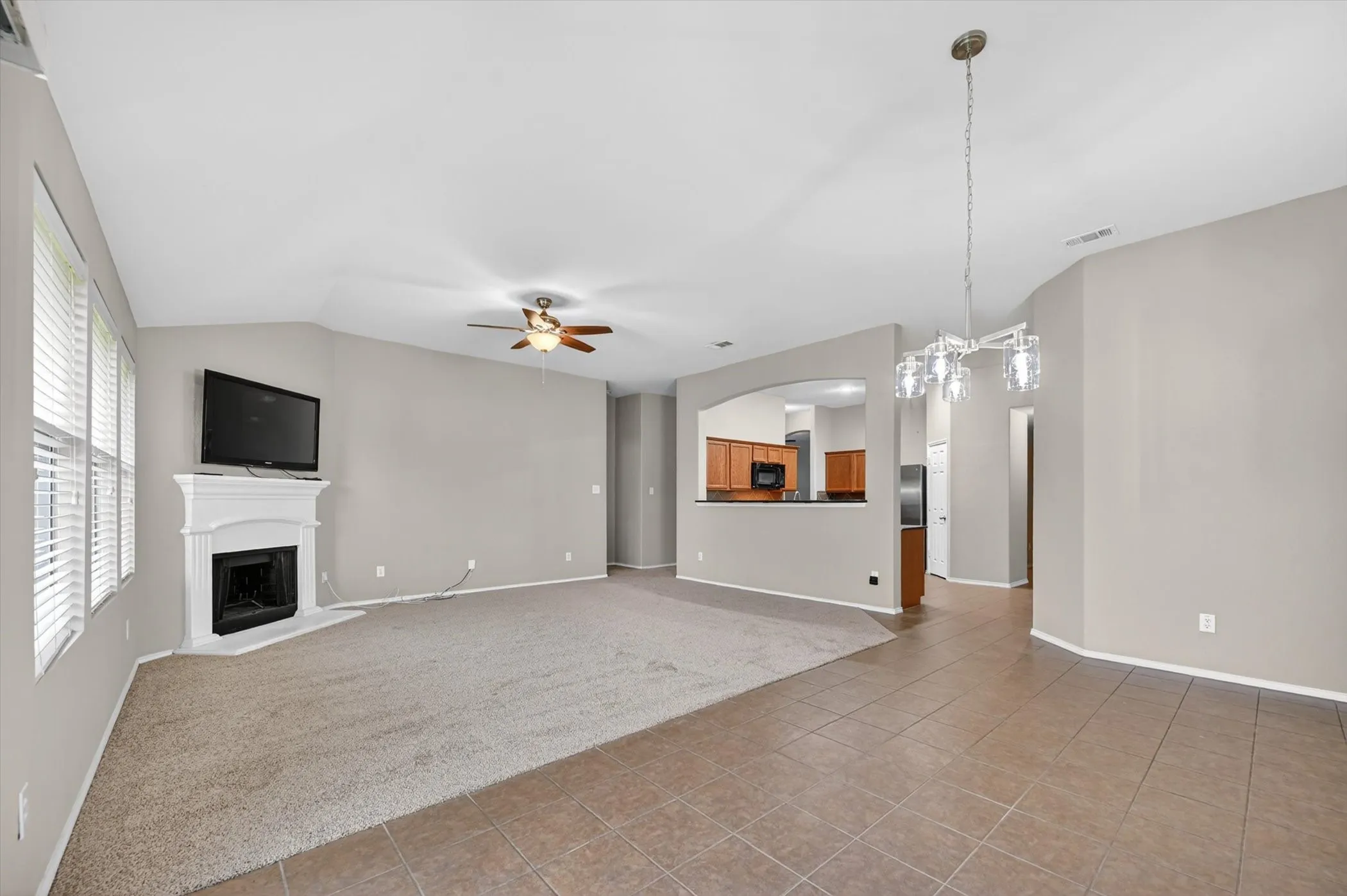 Vaulted ceilings, a built-in corner fireplace, ceiling fan, tile flooring, and a contemporary chandelier