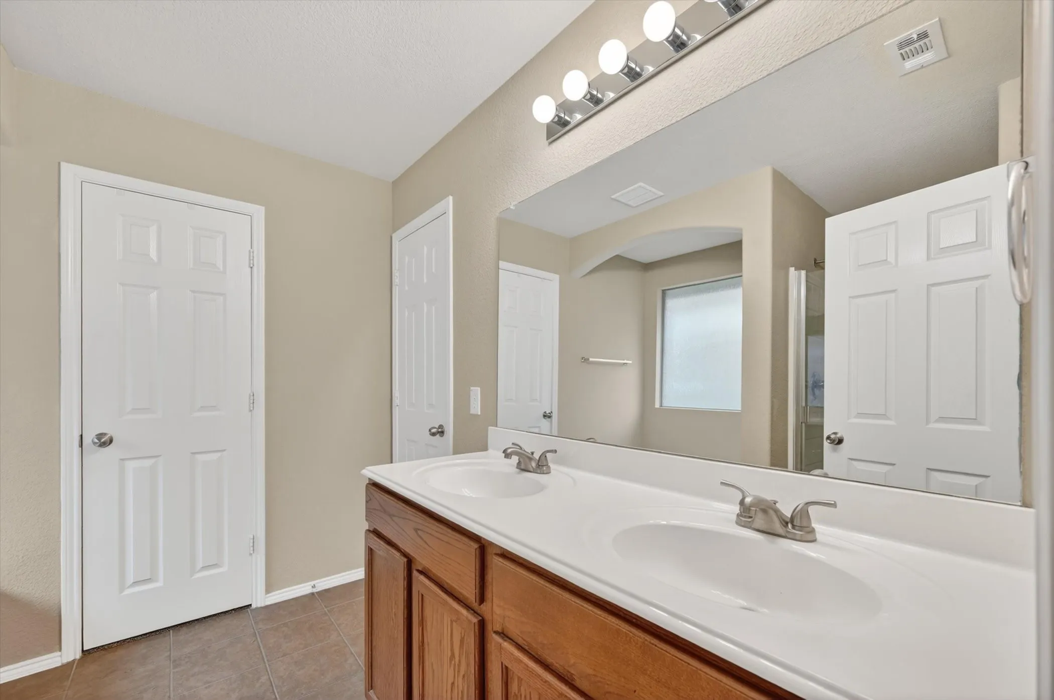 Double vanity with integrated sinks, brushed nickel faucets, wood-finish cabinetry, and a large wall-mounted mirror