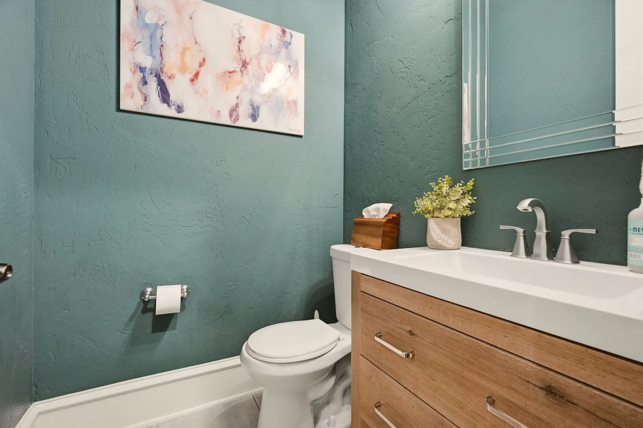 The first floor powder room offers tile floors, a luxurious skip trowel wall texture in a rich green color tone, and a wooden, built-in vanity with brushed nickel hardware, faucet and fixtures.