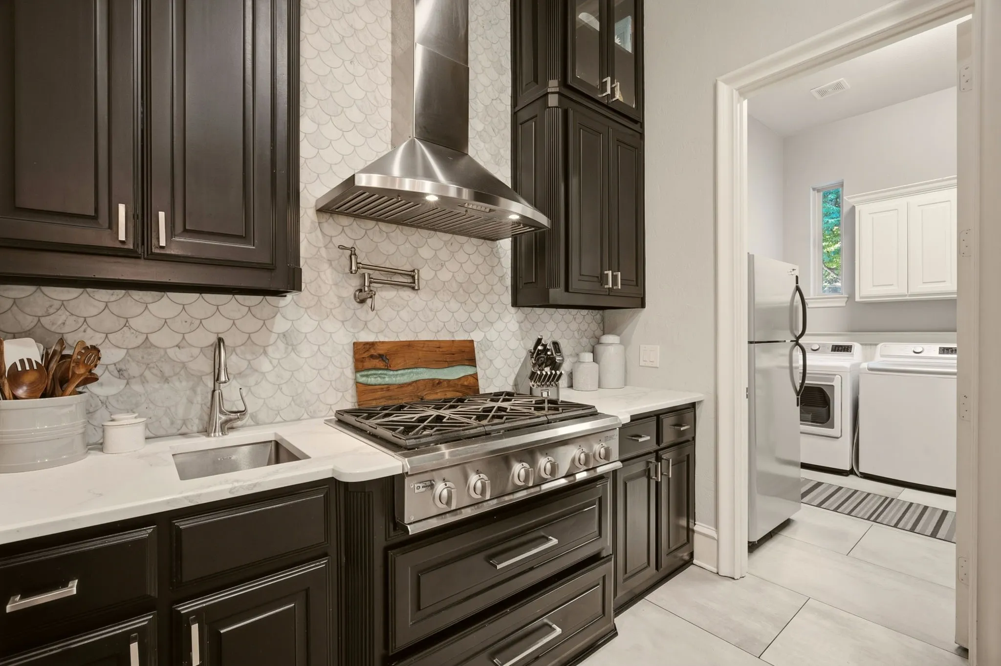 Crisp white quartz countertops with subtle gray veining pair beautifully with a stunning mermaid-style marble backsplash that extends dramatically to the ceiling.
