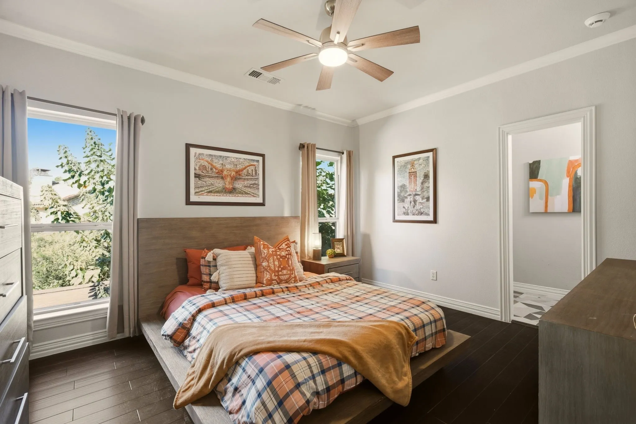 Bedroom 4 offers a bright retreat, featuring wood floors, crown molding, and a ceiling fan. Two tall windows fill the room with natural light, while a spacious walk-in closet with built-in shelving provides exceptional organization and storage.