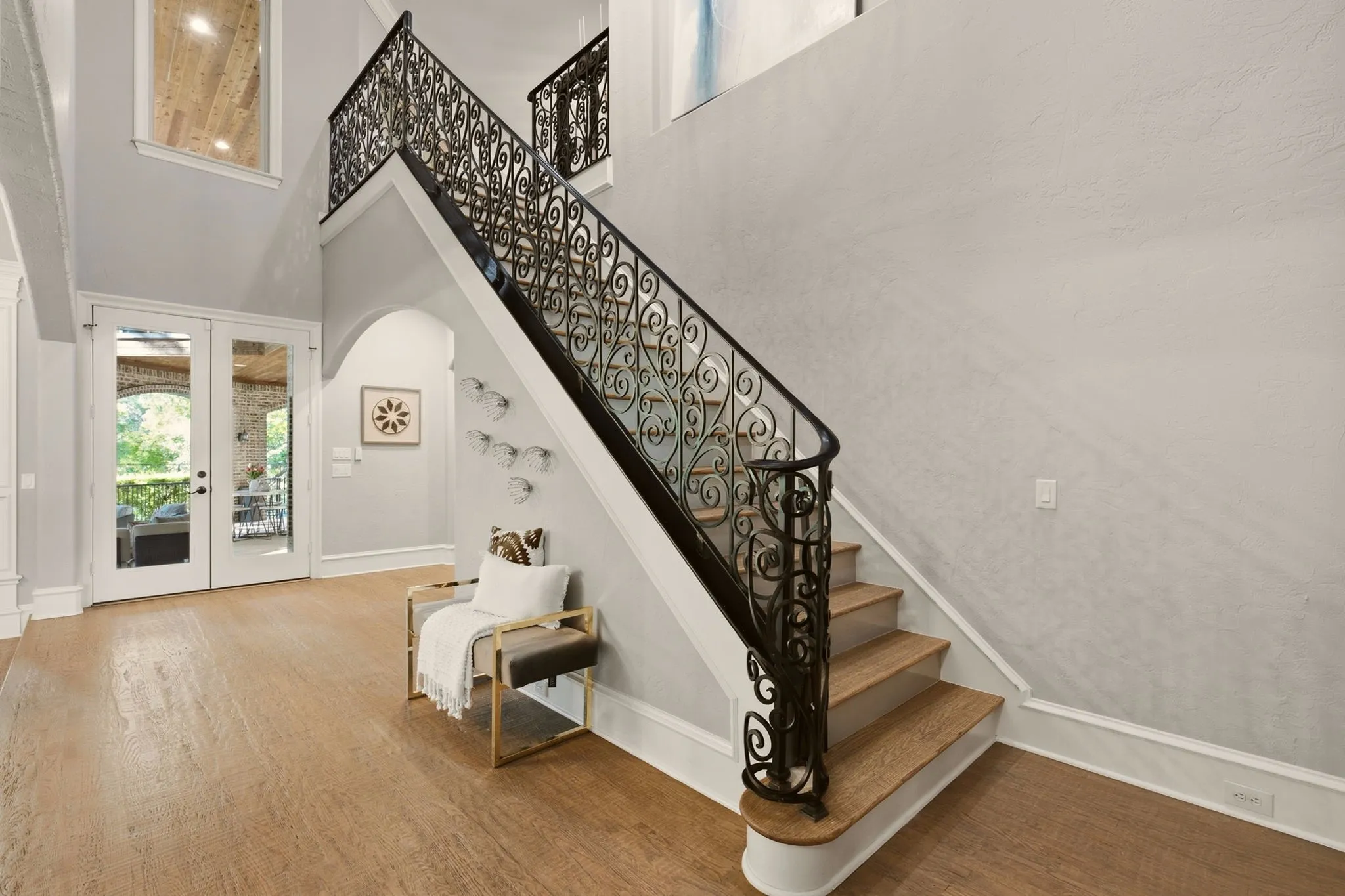 The grand entry makes an unforgettable first impression, soaring beneath 20-foot ceilings and featuring a show-stopping staircase with an elegant wrought-iron volute railing. An awe-inspiring designer chandelier serves as a dramatic focal point, illuminating the hand-scraped hardwood floors below.