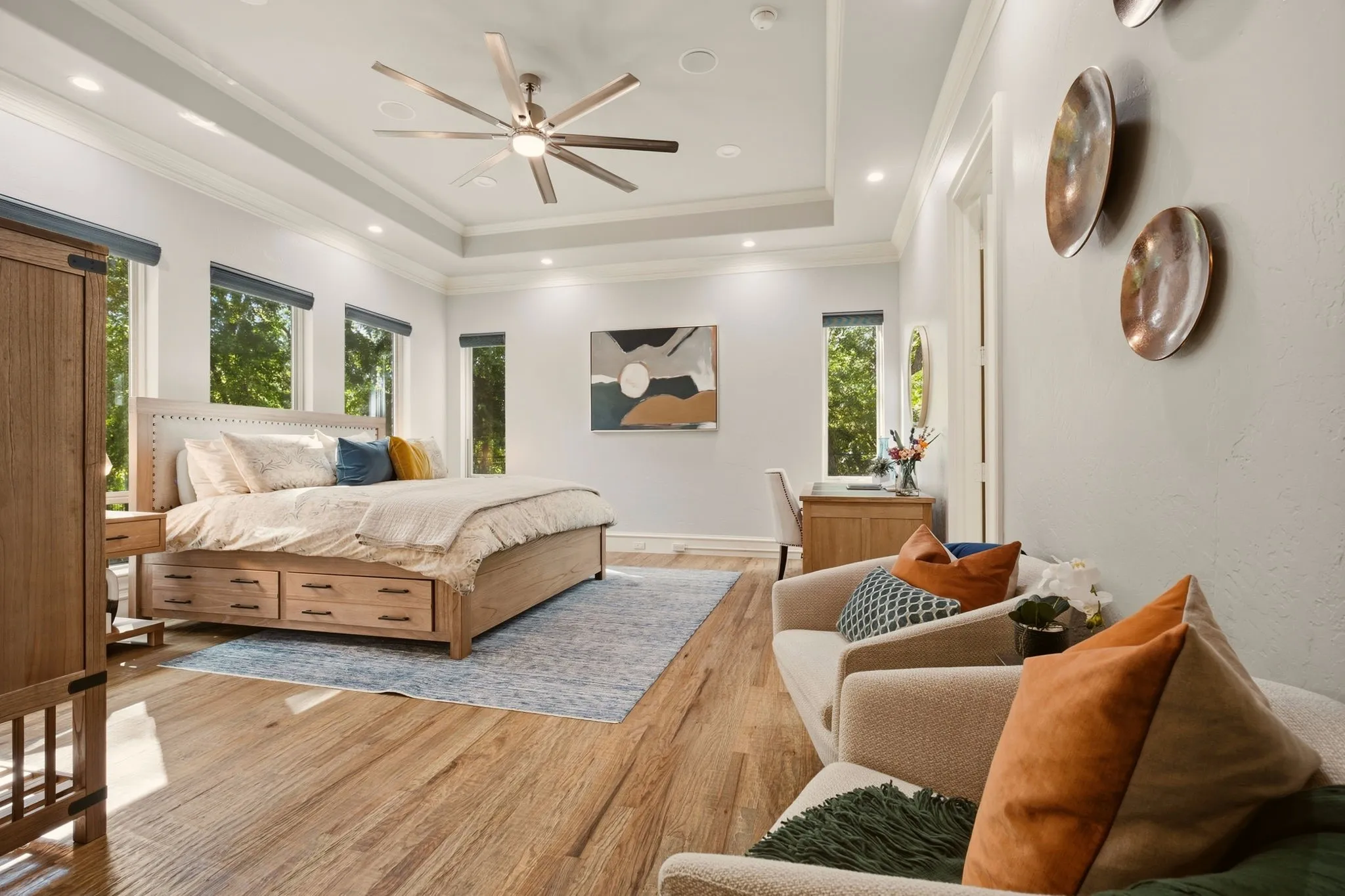 The primary suite is a private retreat designed for comfort and tranquility, offering natural-finish hardwood floors that complement a beautifully detailed tray ceiling accented by double crown molding and a sleek ceiling fan, while integrated in-ceiling speakers add to the relaxing ambiance.