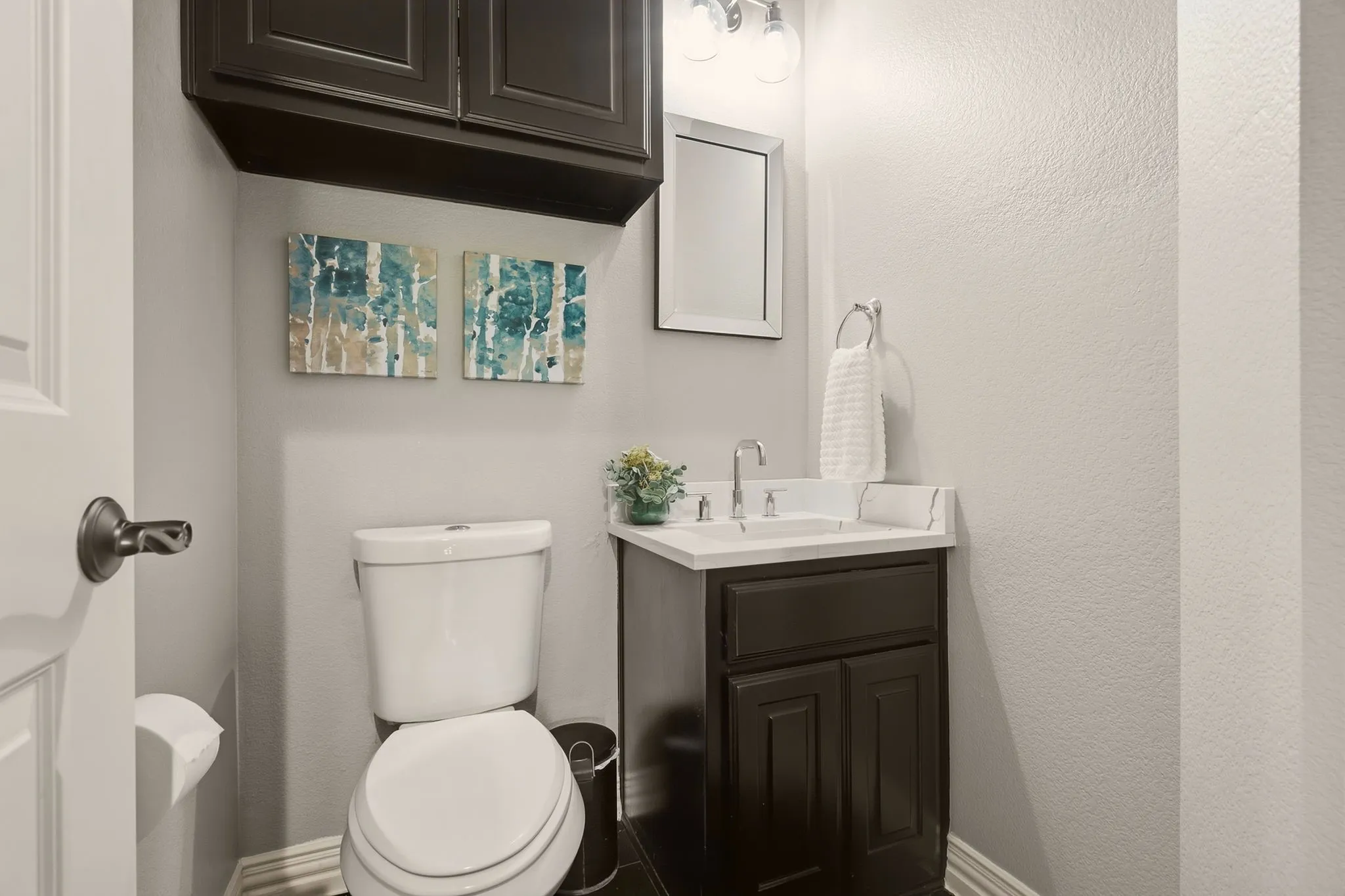 The recently renovated second floor half bathroom offers a space for guests, featuring wood floors, a built-in vanity with quartz countertop and undermount sink, upper cabinets for storage, and crown molding to finish the look.
