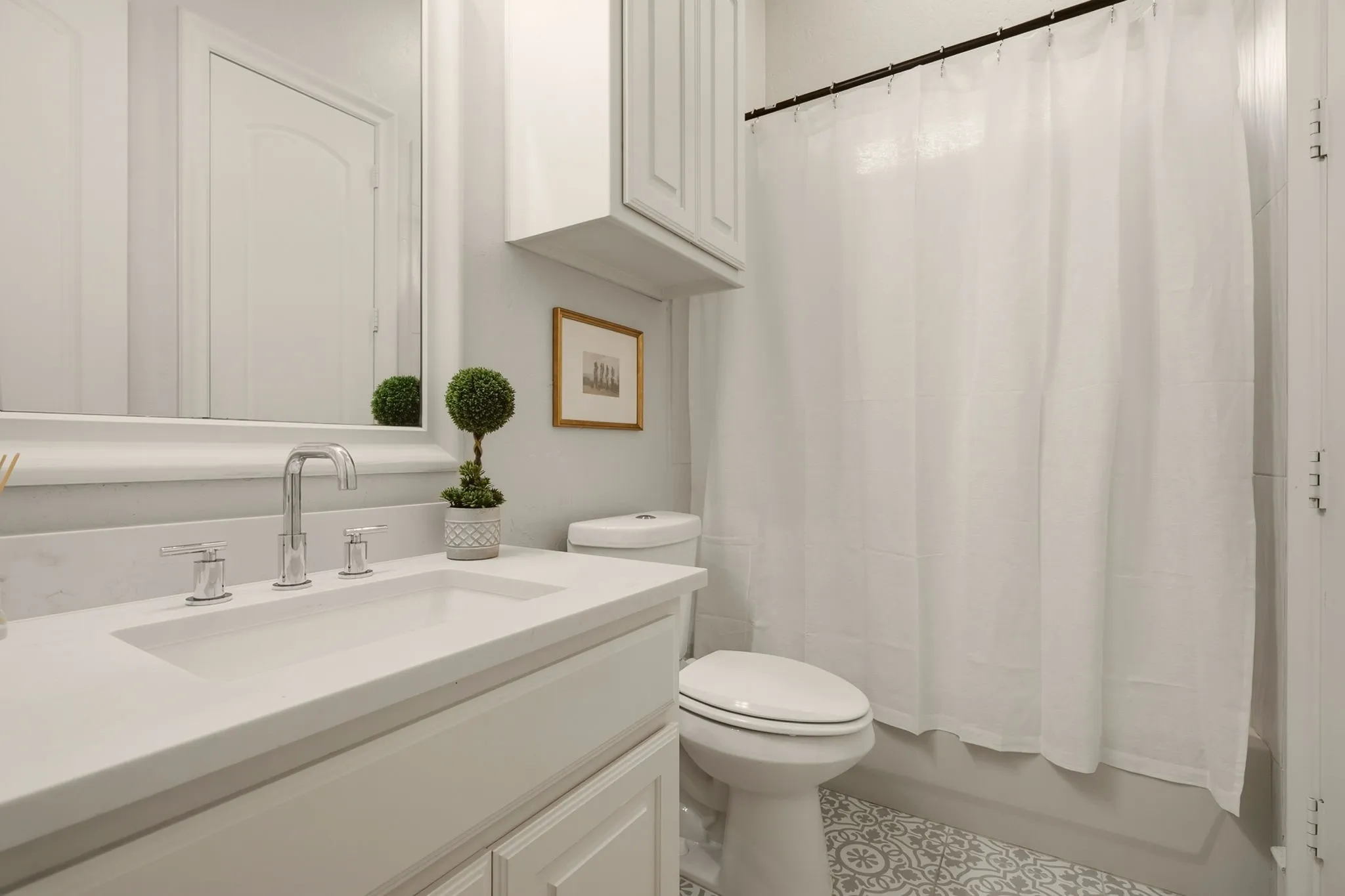 The recently renovated first-floor full bathroom offers convenient dual access from both the guest bedroom and main living area. Whimsical patterned tile flooring adds a touch of personality and charm, complemented by a built-in vanity with an undermount sink, brushed-nickel faucet and fixtures, and coordinating upper cabinetry for additional storage.