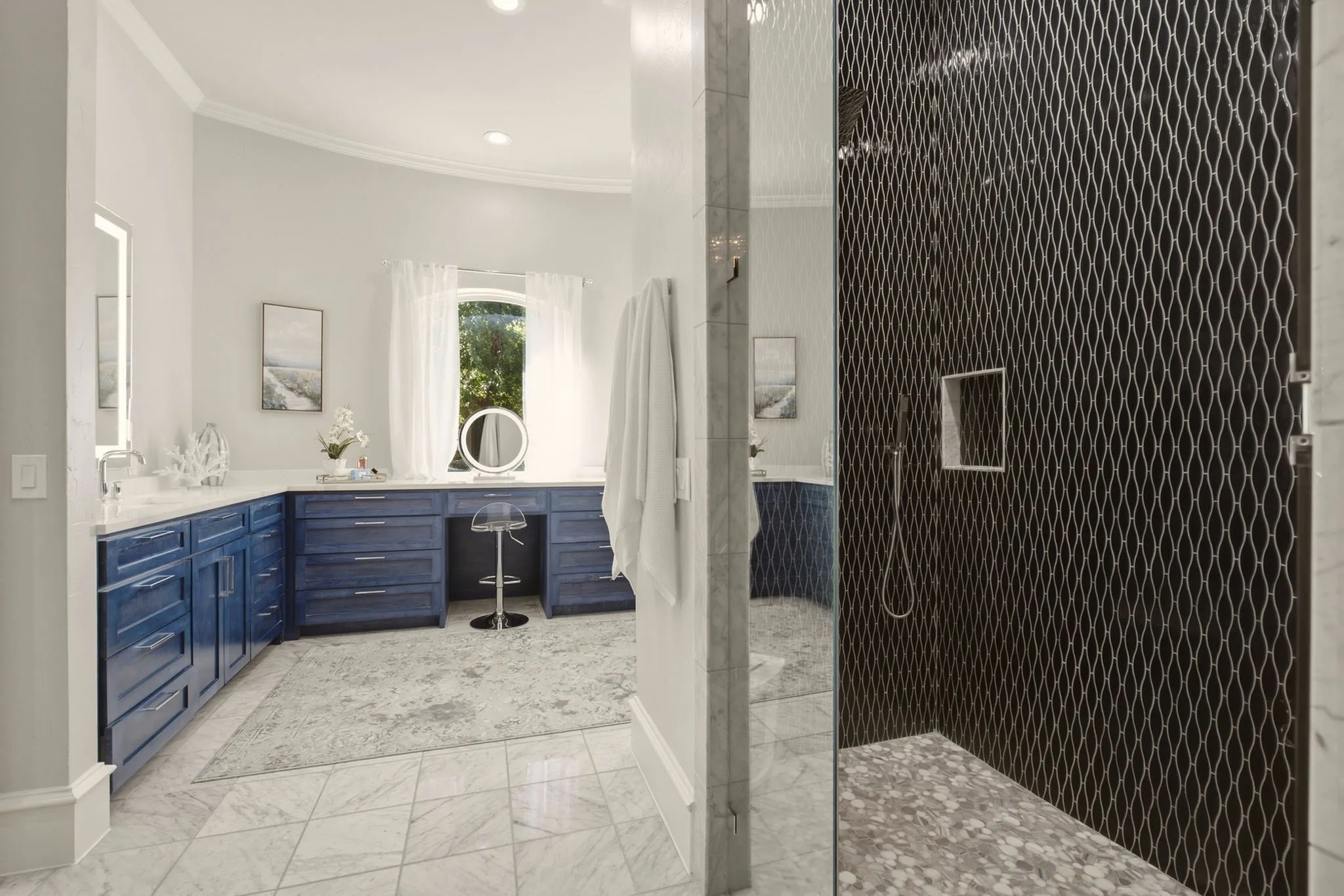 The impressive walk-in shower is enclosed by frameless glass and finished with dramatic floor-to-ceiling black tile. Three rainfall shower heads and an additional body spray create a relaxing showering experience, while two built-in shampoo niches provide sleek, convenient storage.