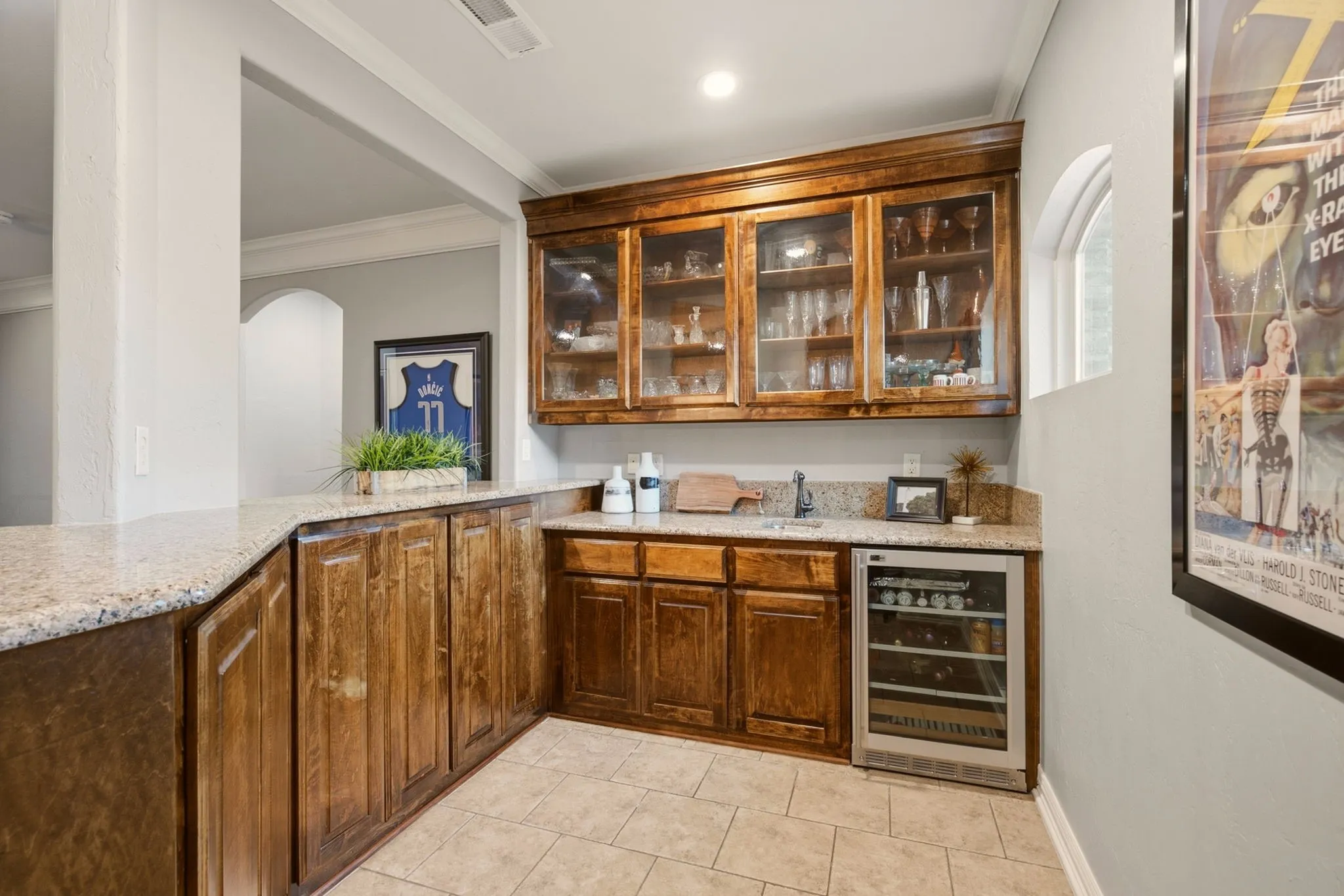 The custom wet bar is thoughtfully designed for effortless entertaining, featuring tile flooring, built-in cabinetry, and glass-front upper cabinets ideal for showcasing a favorite collection of martini and wine glasses.