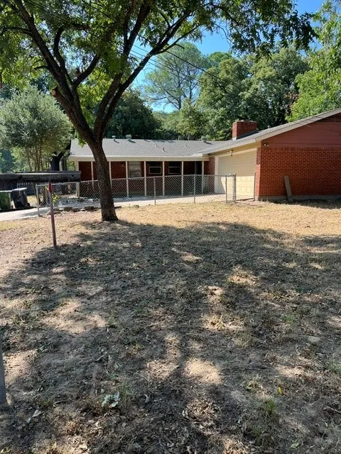 Brick exterior with a covered patio, chain-link fencing, and an attached garage with a panel door
